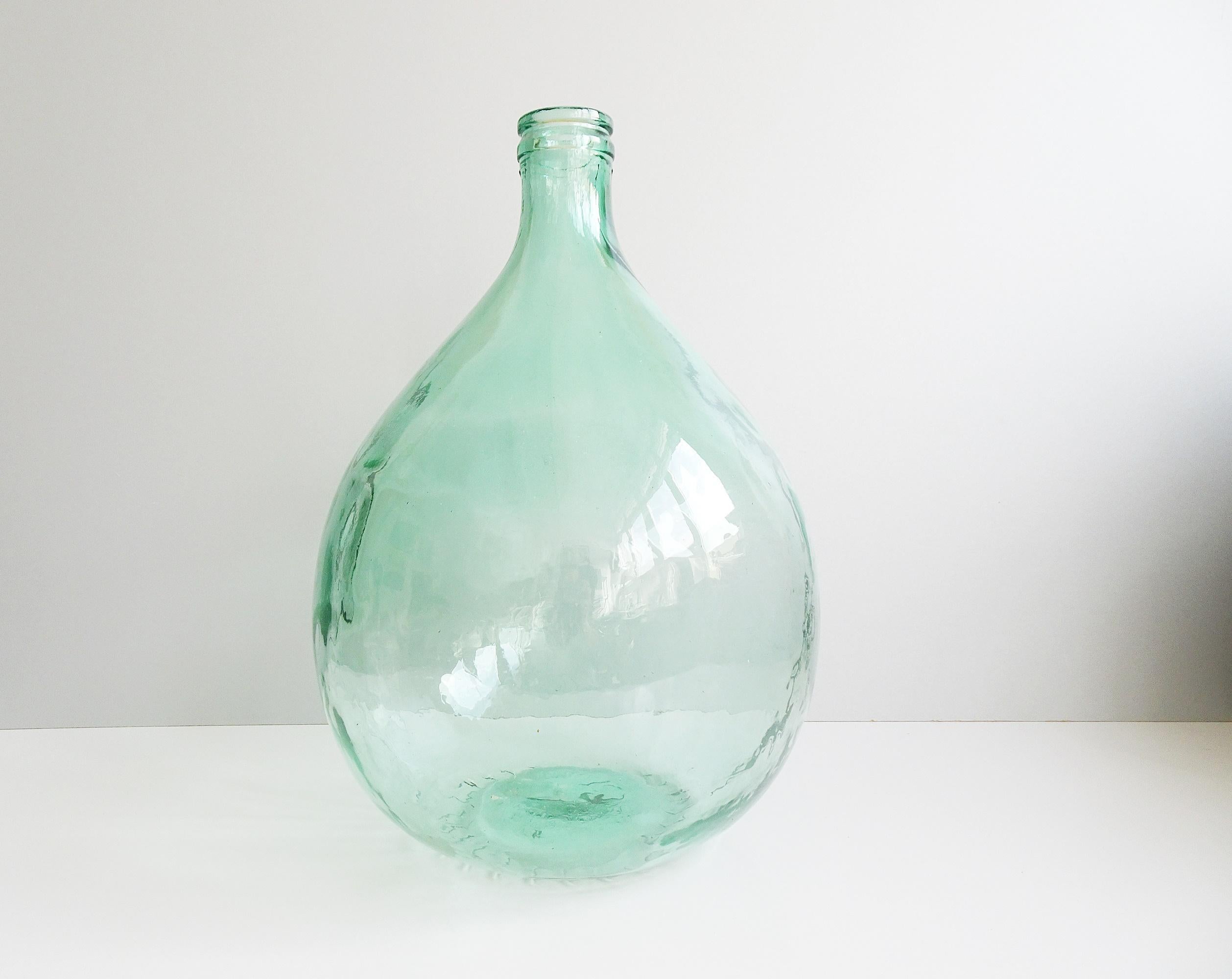 This large light turquoise demijohn is a classic French demijohn from the 1950s. Light green / turquoise pressed glass with visible air pockets. A timeless home decor to set accents, as a floor vase with dried flowers, light catcher, alone or in
