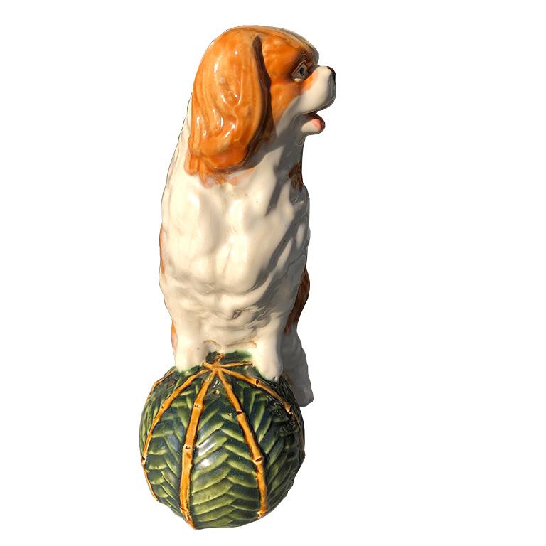 One dog with ball statue in the style of Staffordshire. Beautiful spaniel stands with front legs on top of a green and bamboo pattern ball. Spaniel is orange and cream in color. Would be a beautiful piece to add to a collection of similar pieces.