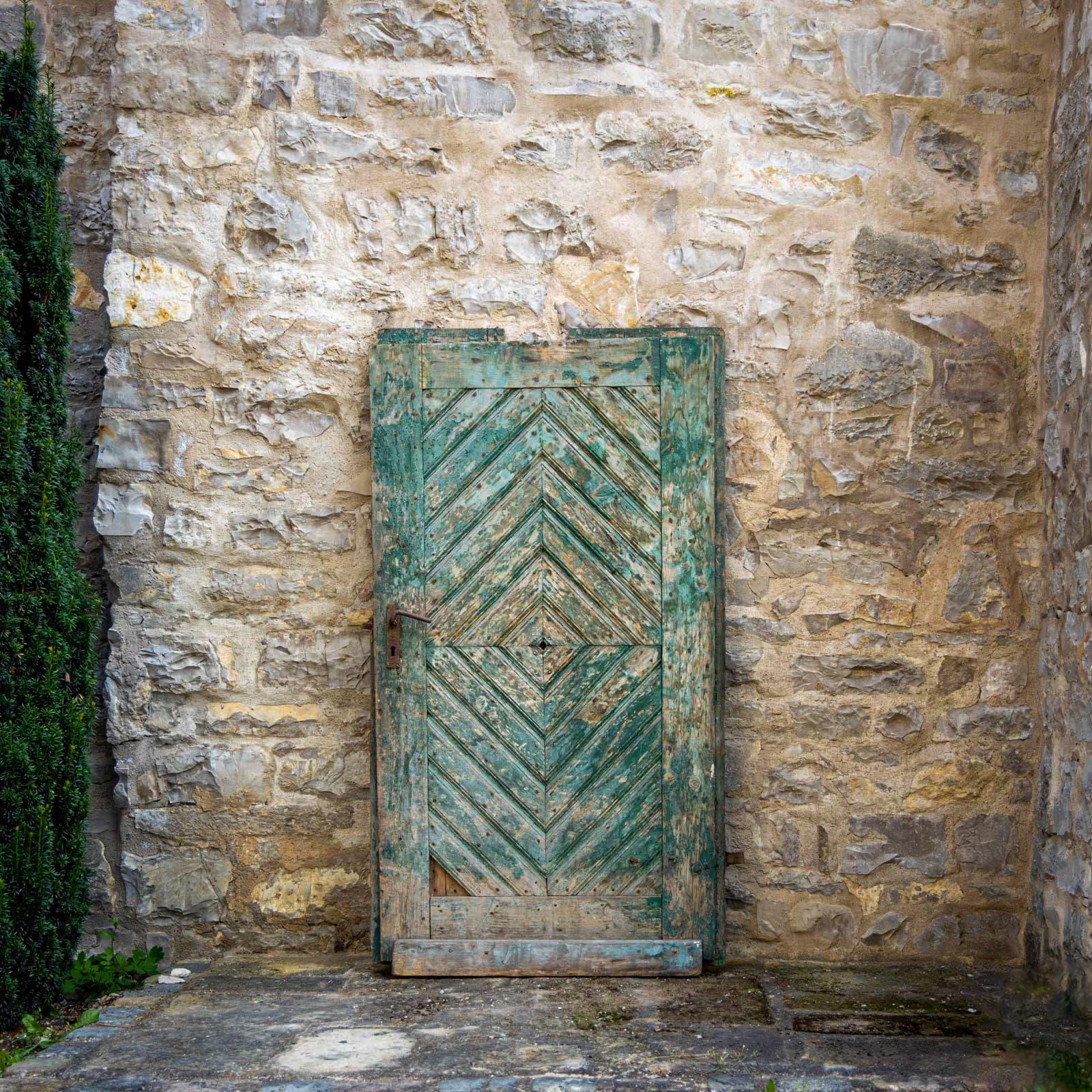 Puerta de madera antigua con marco verde antiguo y diseño de chevron. 