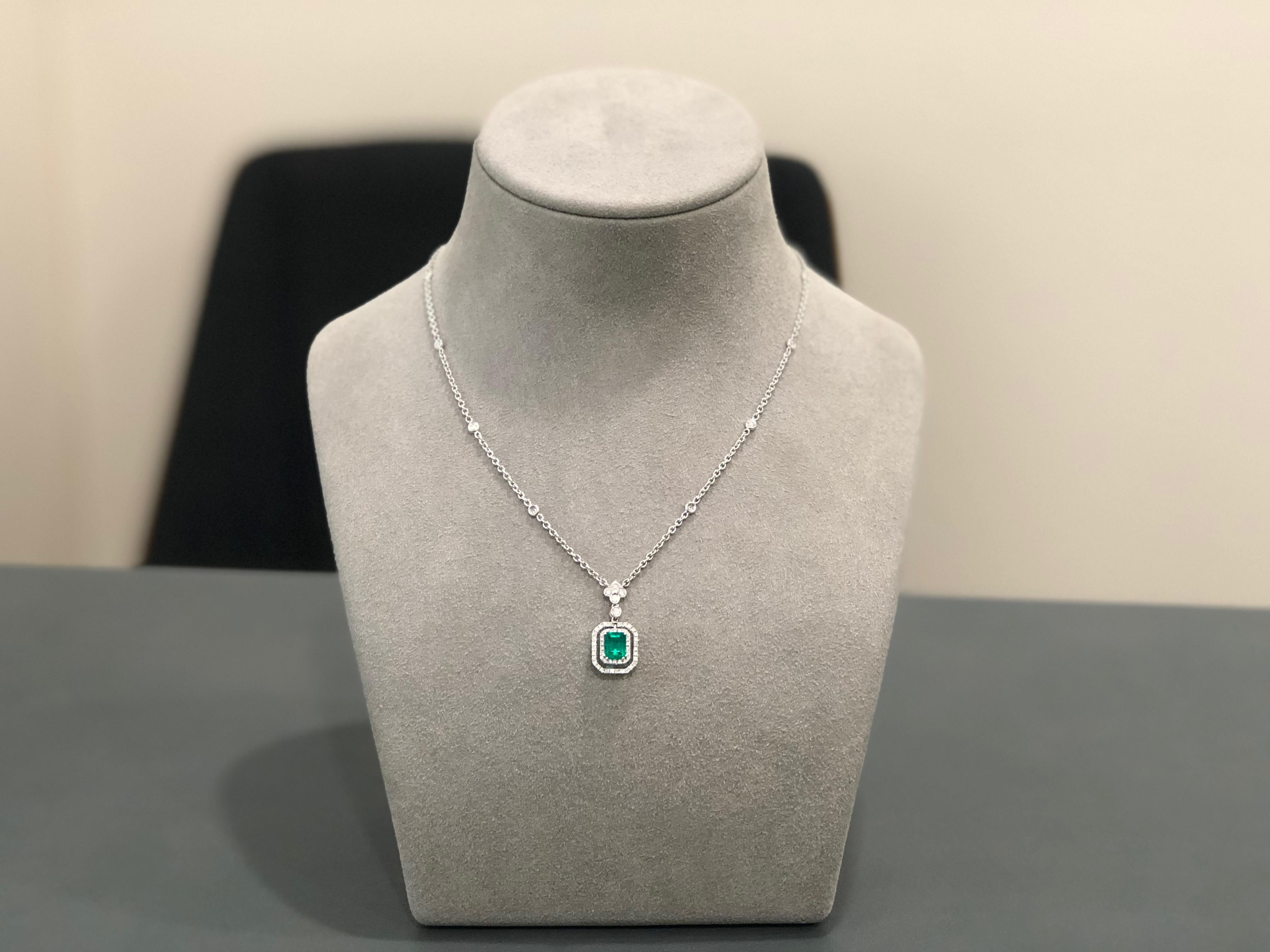Elegant pendant set with a green emerald cut emerald center; surrounded by a two rows of round diamonds. The emerald weighs 1.04 carats. Pendant spaced by a bezel set round diamond. 4 Bezel set round diamond surmount with a 16 inch 18k white gold
