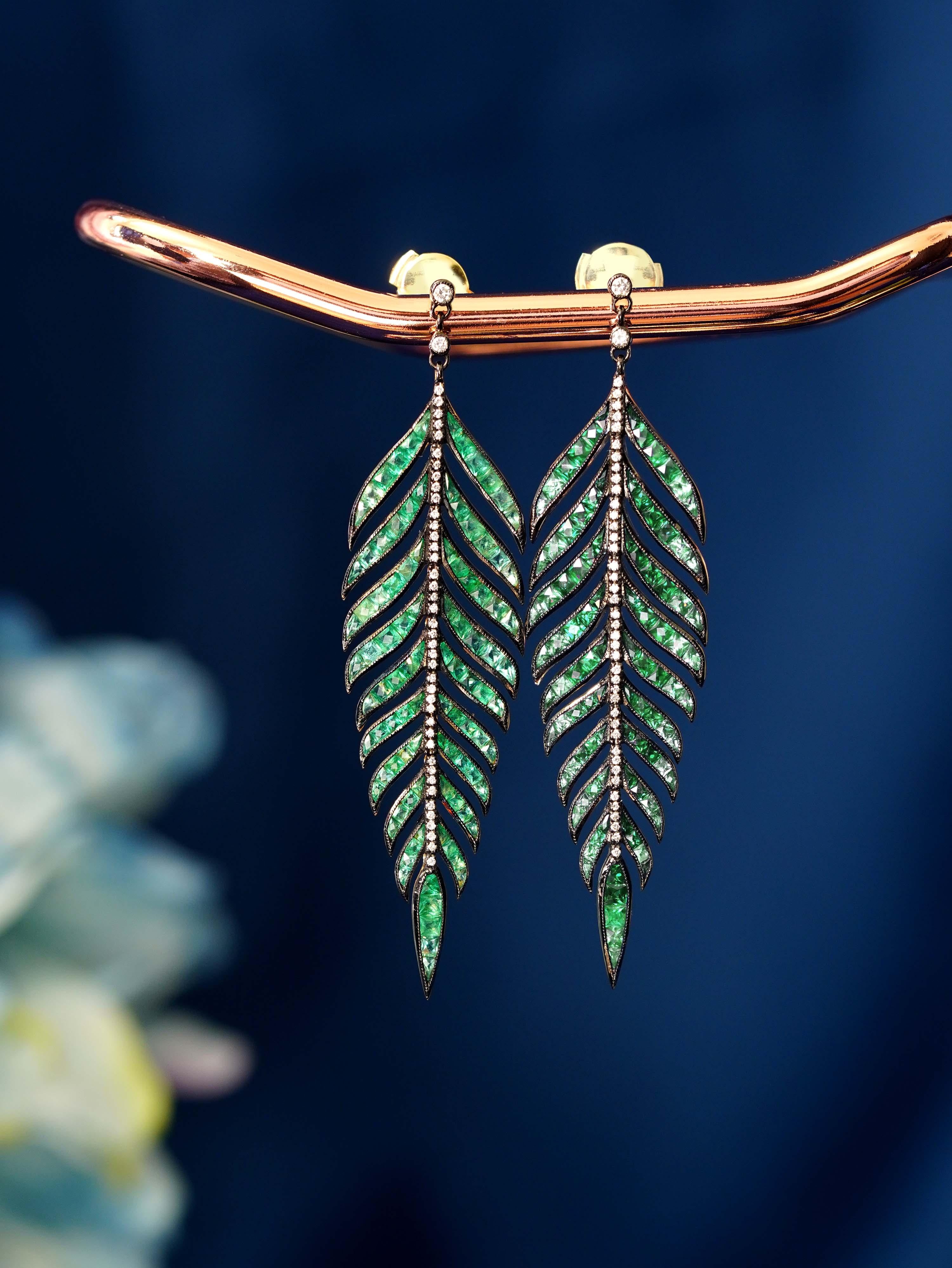 The essence of vintage elegance with a touch of nature’s beauty. Each earring features a vibrant emerald, delicately nestled within a swirling leaf design that shimmers with diamond accents. The graceful curves and intricate detailing create a sense