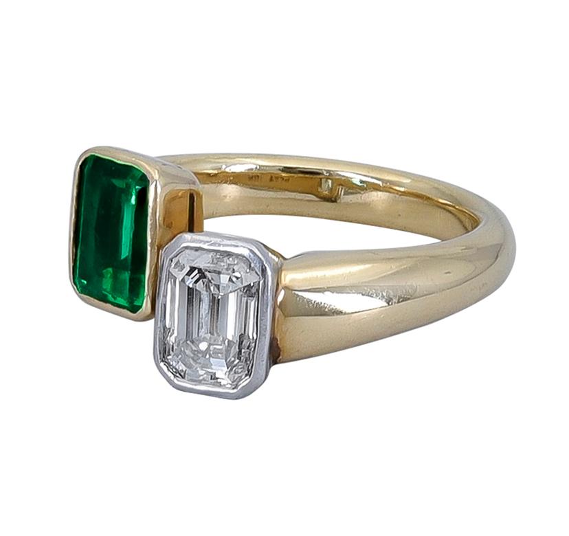 A beautiful crossover/bypass ring design from the 1970's showcasing a vibrant green emerald and an emerald cut diamond in a platinum / 18k yellow gold mounting. 
Total weight of both stones is 1.60 carats.
The ring is 0.11 - 0.28 inches thick.
Size