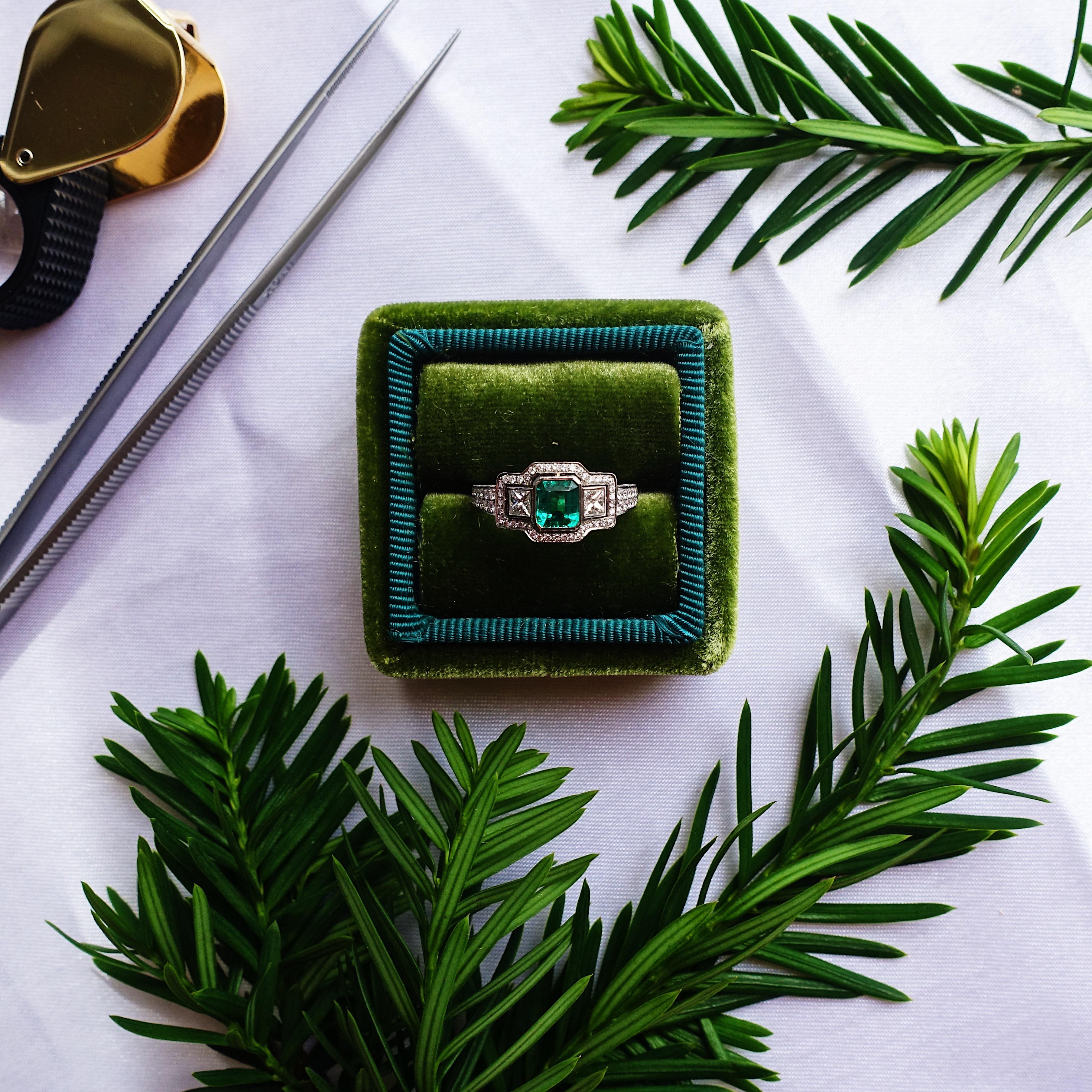 A darling and delicate, traditional style, newly made estate style emerald engagement ring crafted in platinum. The ring centers one bright pure green emerald framed by high polished bezel and flanked by princess and round cut diamonds. Outlining
