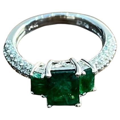 This exquisite ring is crafted with precision, featuring a striking central emerald flanked by two additional emeralds. The band is adorned with a series of sparkling diamonds, enhancing its luxurious appeal. The craftsmanship reflects the expertise