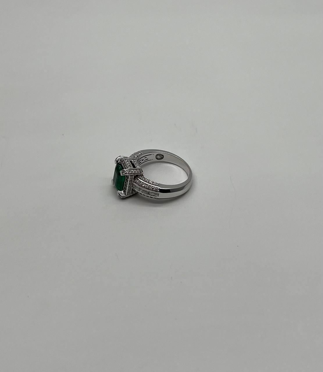 A study in elegance, contrast, and brilliance.
This striking ring features a captivating deep green emerald-cut center emerald. The vibrant gem is framed by a series of sparkling white diamonds, enhancing its rich hue. The diamonds extend along the