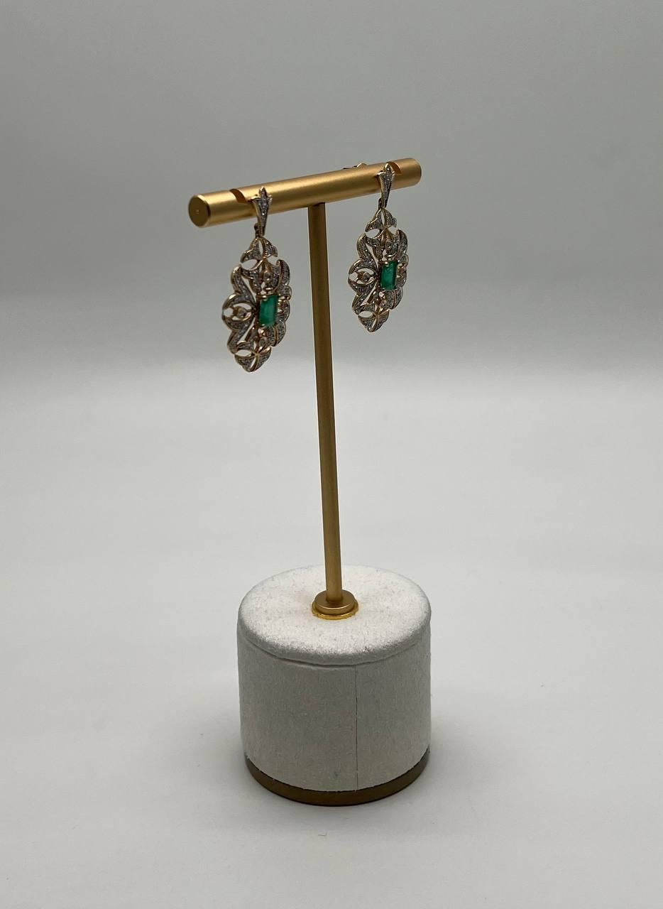 Questa coppia di gioielli è caratterizzata da un'intricata lavorazione in filigrana con uno smeraldo verde centrale. Gli orecchini sono realizzati con attenzione ai dettagli e mostrano una miscela armoniosa di texture e forme. Sono in ottime