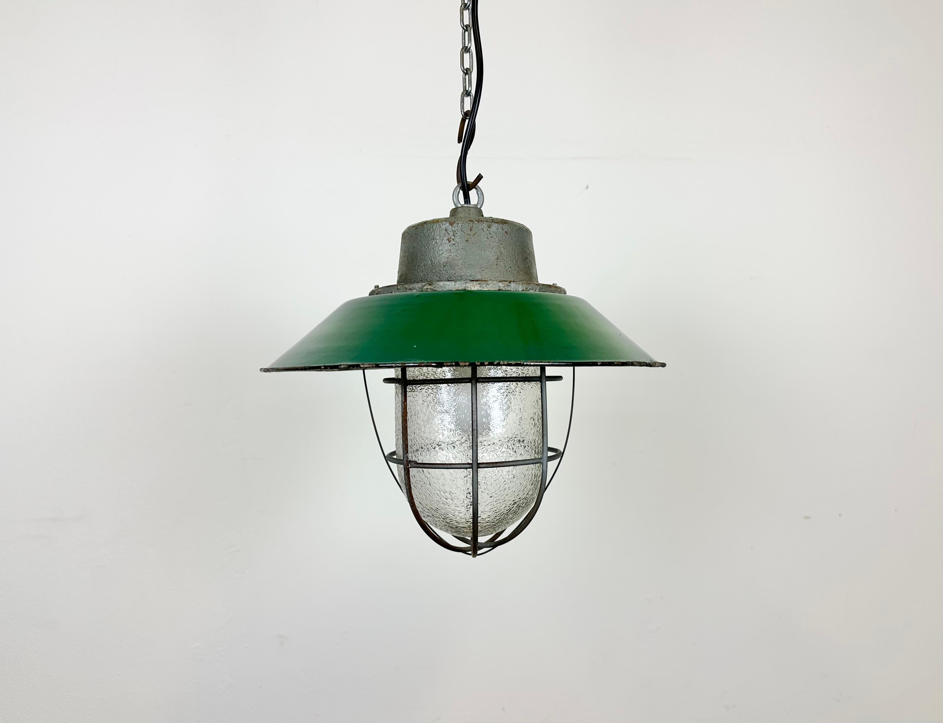 Industrial hanging lamp manufactured in Poland during the 1960s. It features a green enamel shade with white enamel interior, a cast iron top,a frosted glass cover and iron grid. The porcelain socket requires E 27/ E26 lightbulbs .New wire. The
