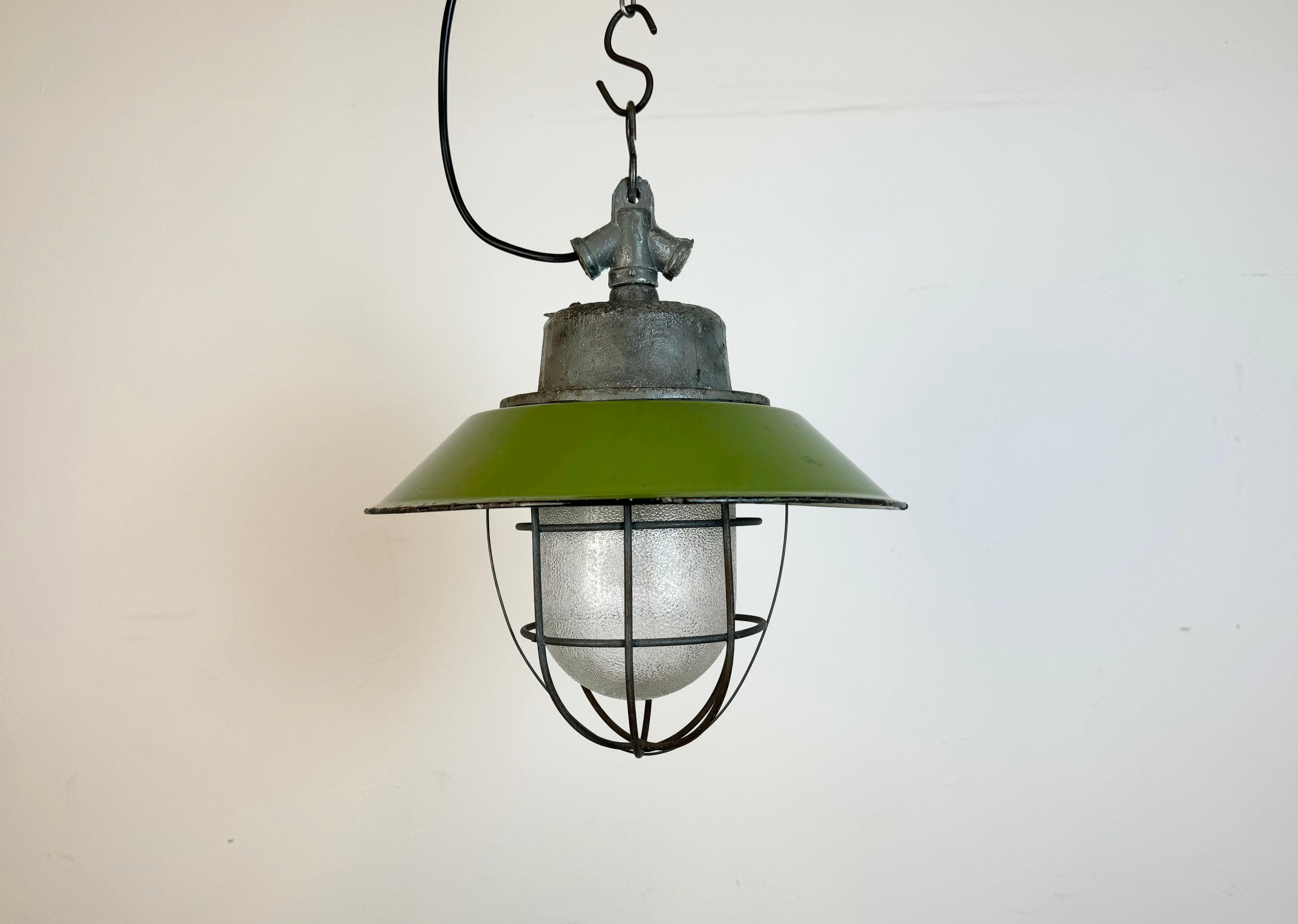 Industrial hanging lamp manufactured in Poland during the 1960s. It features a green enamel shade with white enamel interior, a cast iron top,a frosted glass cover and iron grid. The porcelain socket requires standard E 27/ E26 lightbulbs .New wire.