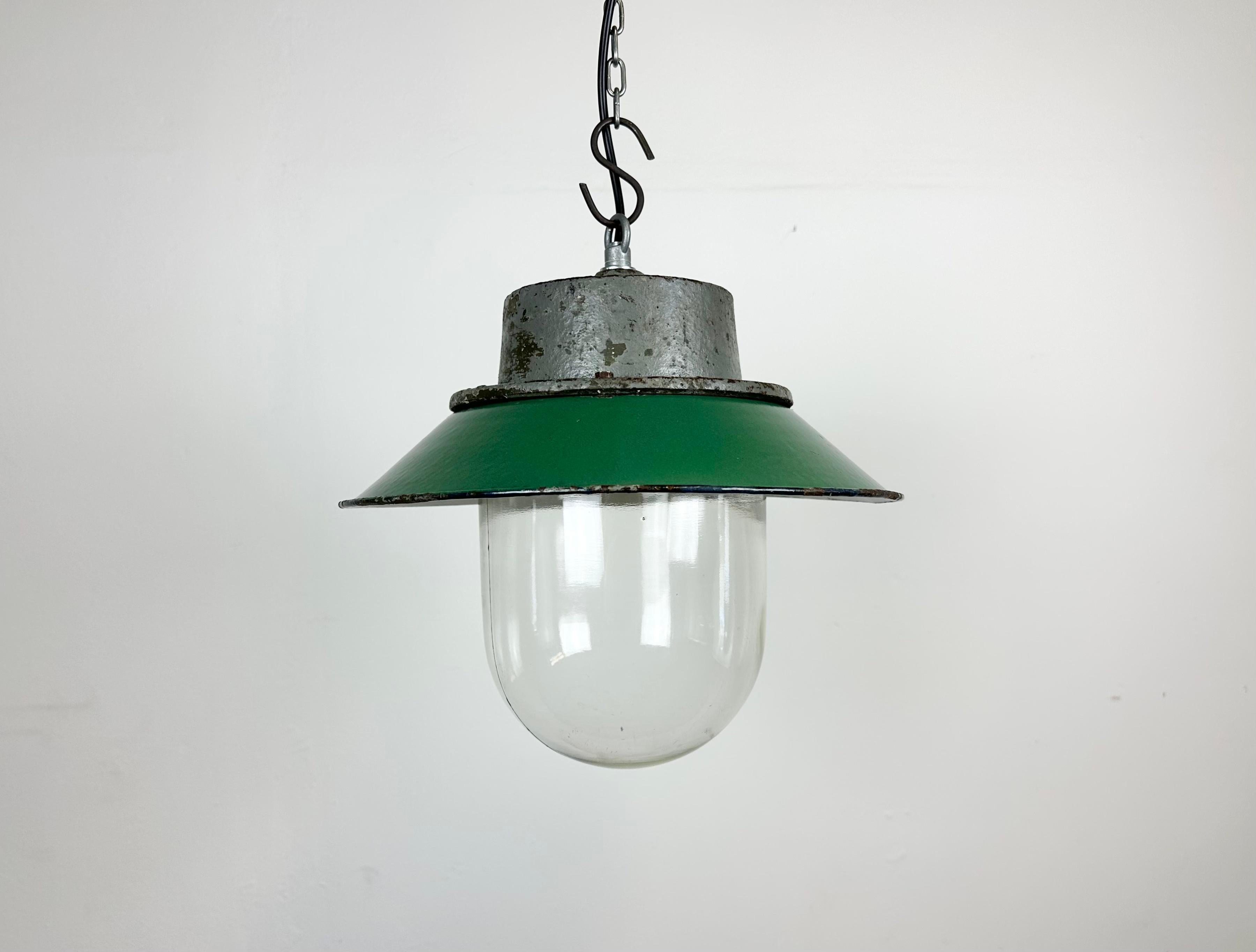 Industrial hanging lamp manufactured in Poland during the 1960s. It features a green enamel shade with a white enamel interior, a grey cast iron top, and a clear glass cover. The porcelain socket requires E 27/ E26 lightbulbs. New wire. The weight