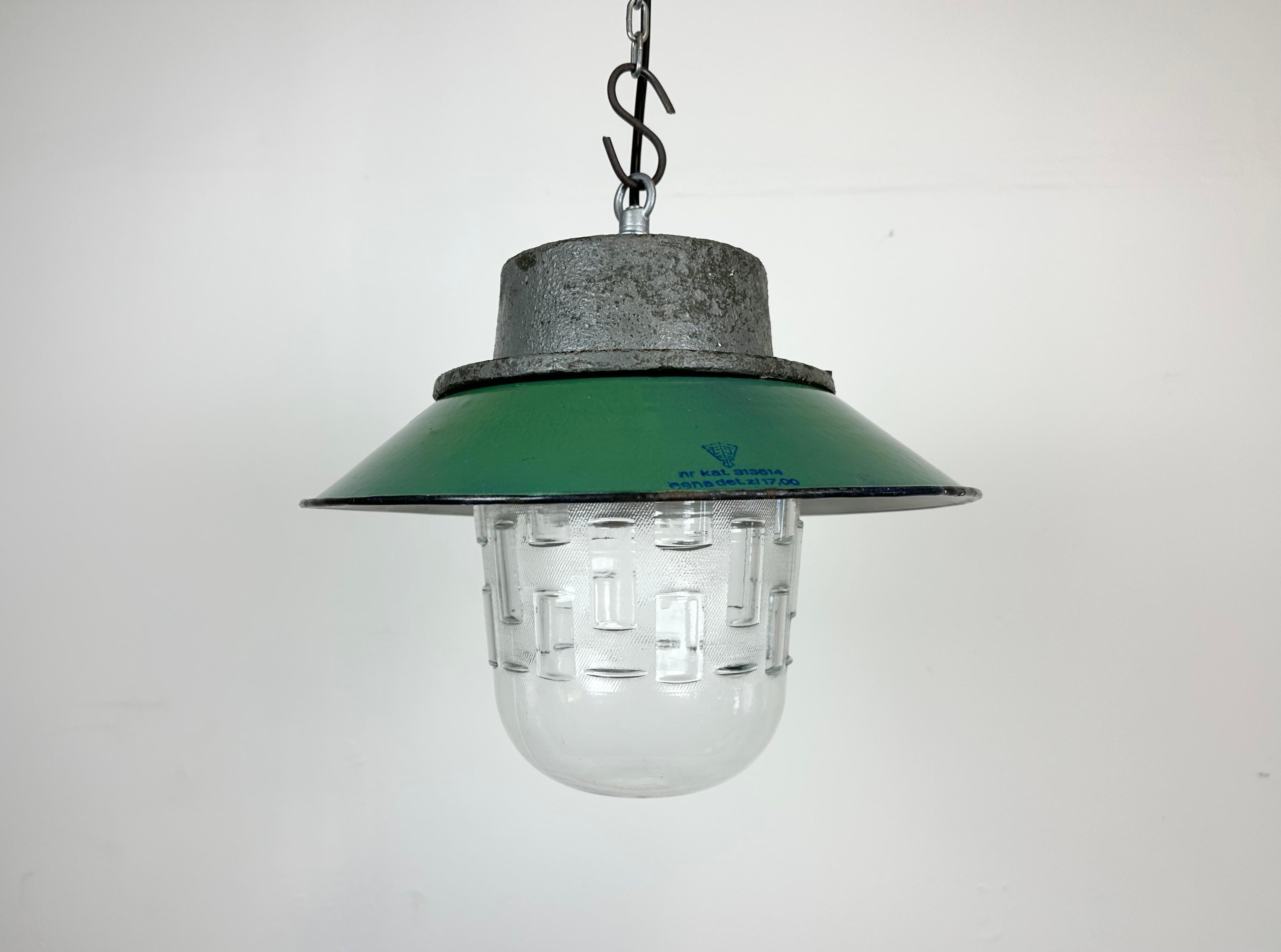 Industrial hanging lamp manufactured in Poland during the 1960s. It features a green enamel shade with white enamel interior, a cast iron top and a glass cover. The porcelain socket requires E 27/ E26 lightbulbs .New wire. The weight of the lamp is