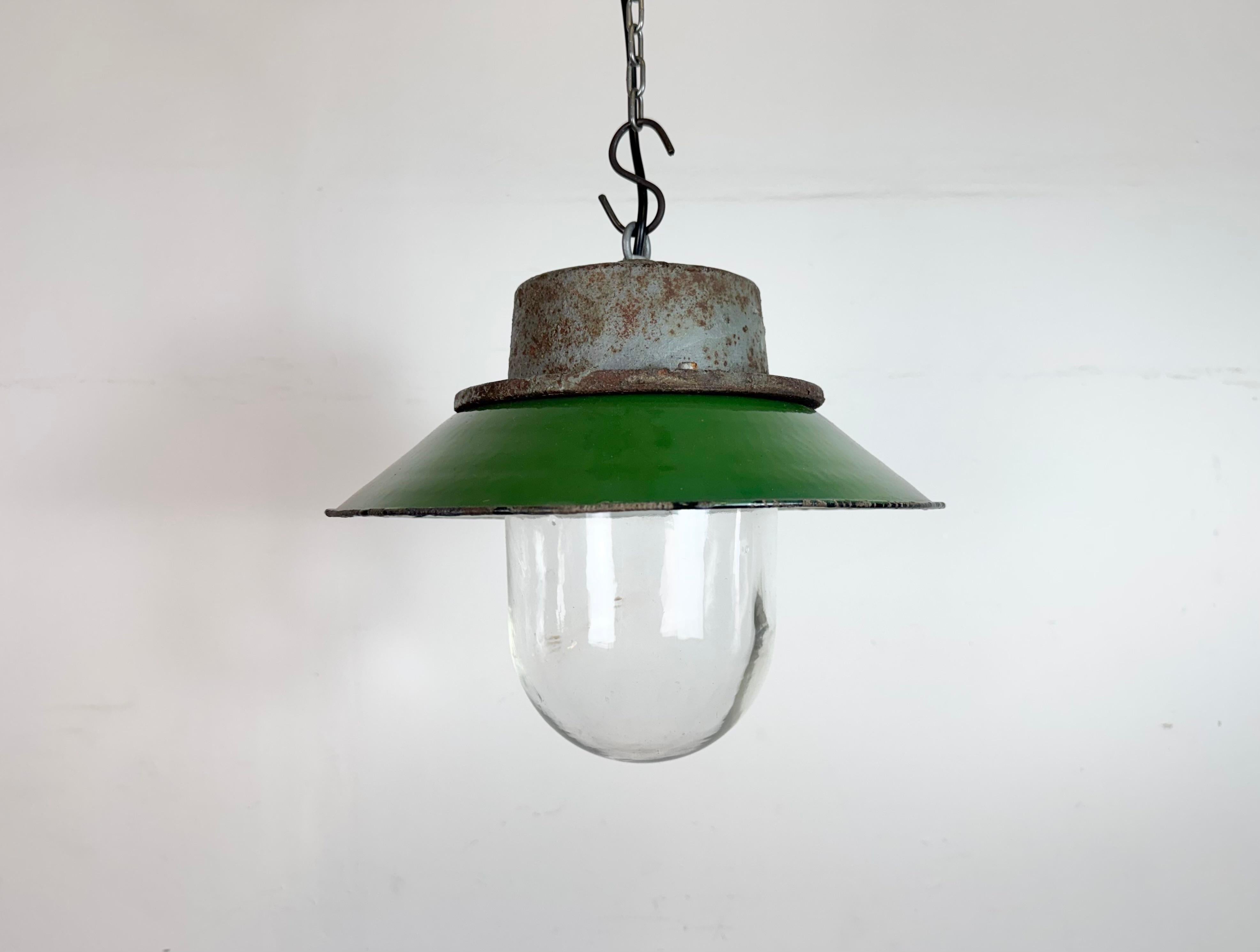 Industrial hanging lamp manufactured in Poland during the 1960s. It features a green enamel shade with a white enamel interior, a grey cast iron top, and a clear glass cover. The porcelain socket requires E 27/ E26 lightbulbs. New wire. The weight