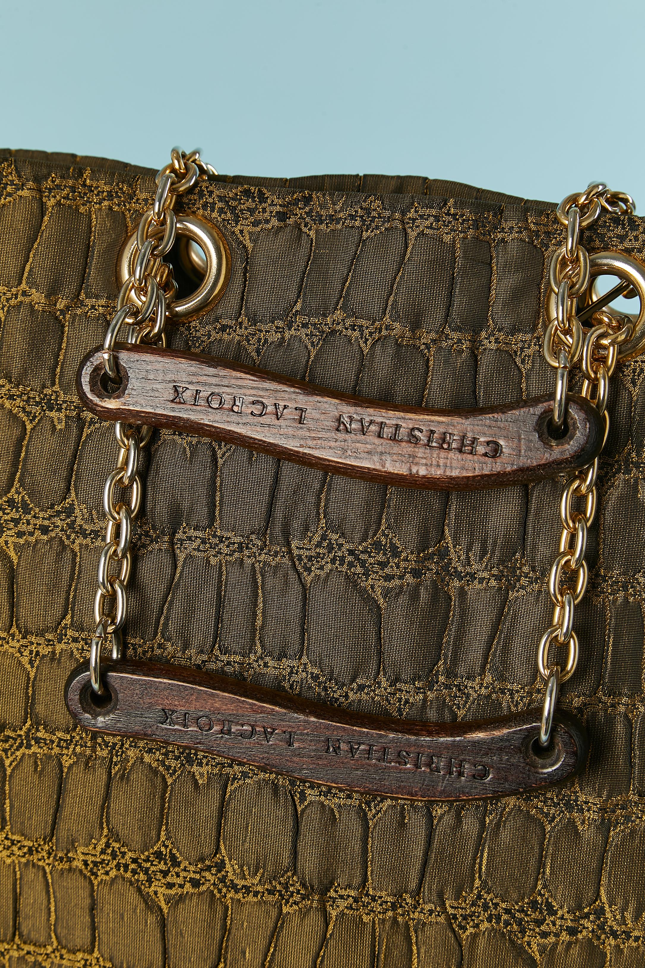 Sac à anse en tissu vert (probablement de la rayonne) avec motif de crocodile. Poignée en bois marquée + chaîne et œillet en métal doré. 
Doublure en plastique noir et une poche avec fermeture à glissière à l'intérieur. 
TAILLE 30 cm X 29 cm X 10 cm