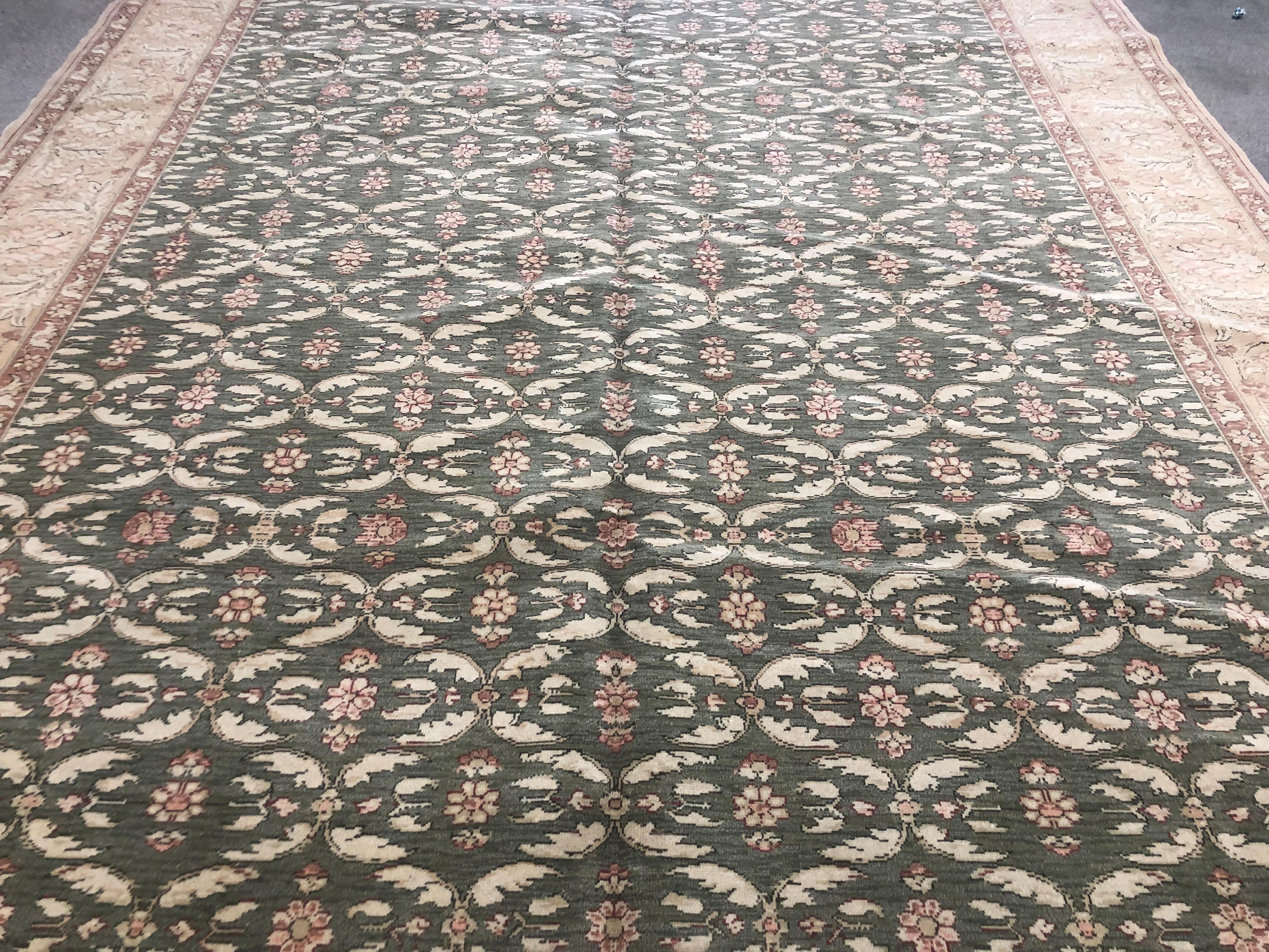 A cream and pink lattice of flowers stands out against a green 'grass' background in this endearing wool area rug. A beige floral border and red floral ribbons frame the image. Hand knotted wool.