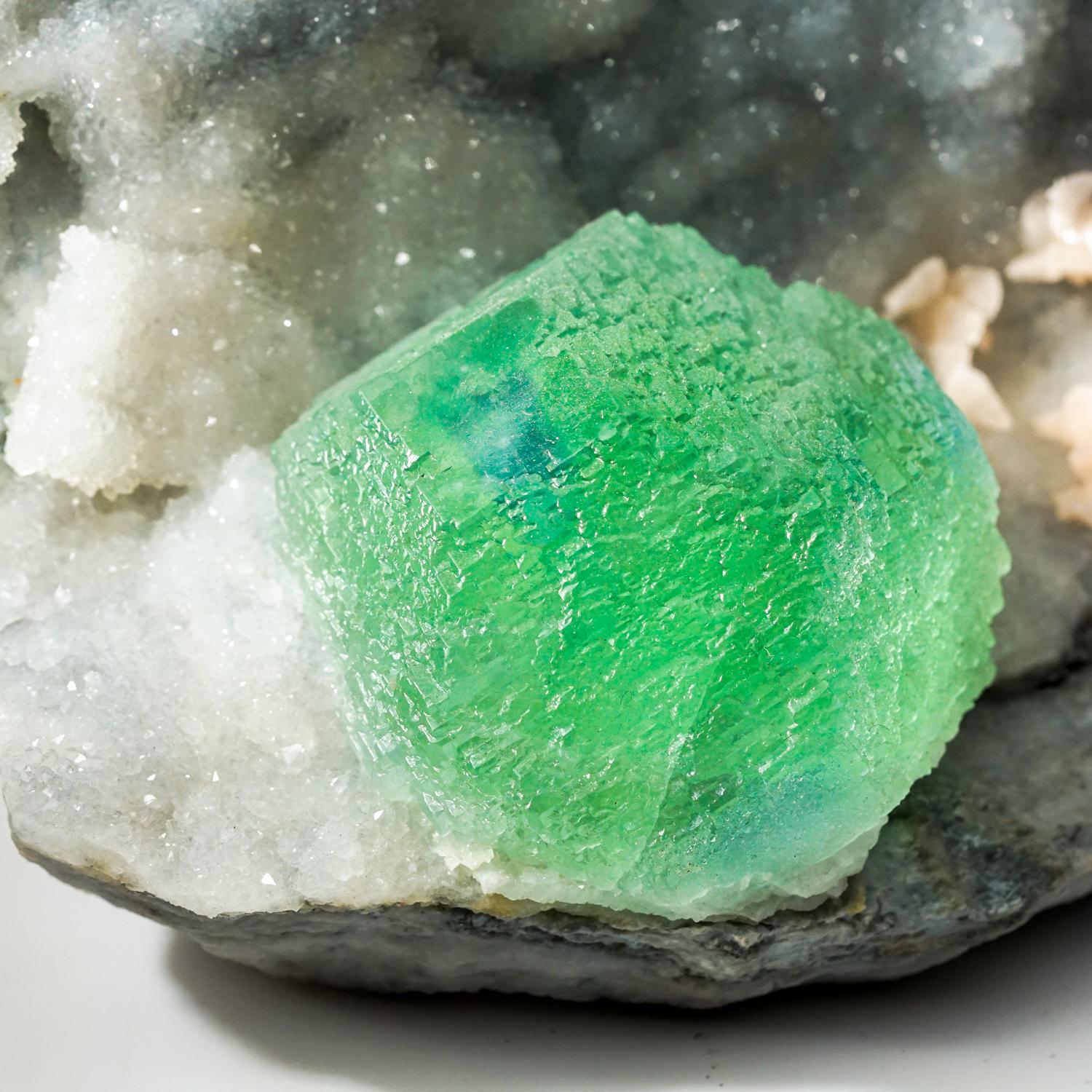 From Ruyuan, Lechang, Guandong, China

Large showy 1.5 inch gem green transparent fluorite crystal with blue phantom zoning at the center termination on matrix lined with scintillating quartz with peach dolomite crystals. The fluorite has lustrous