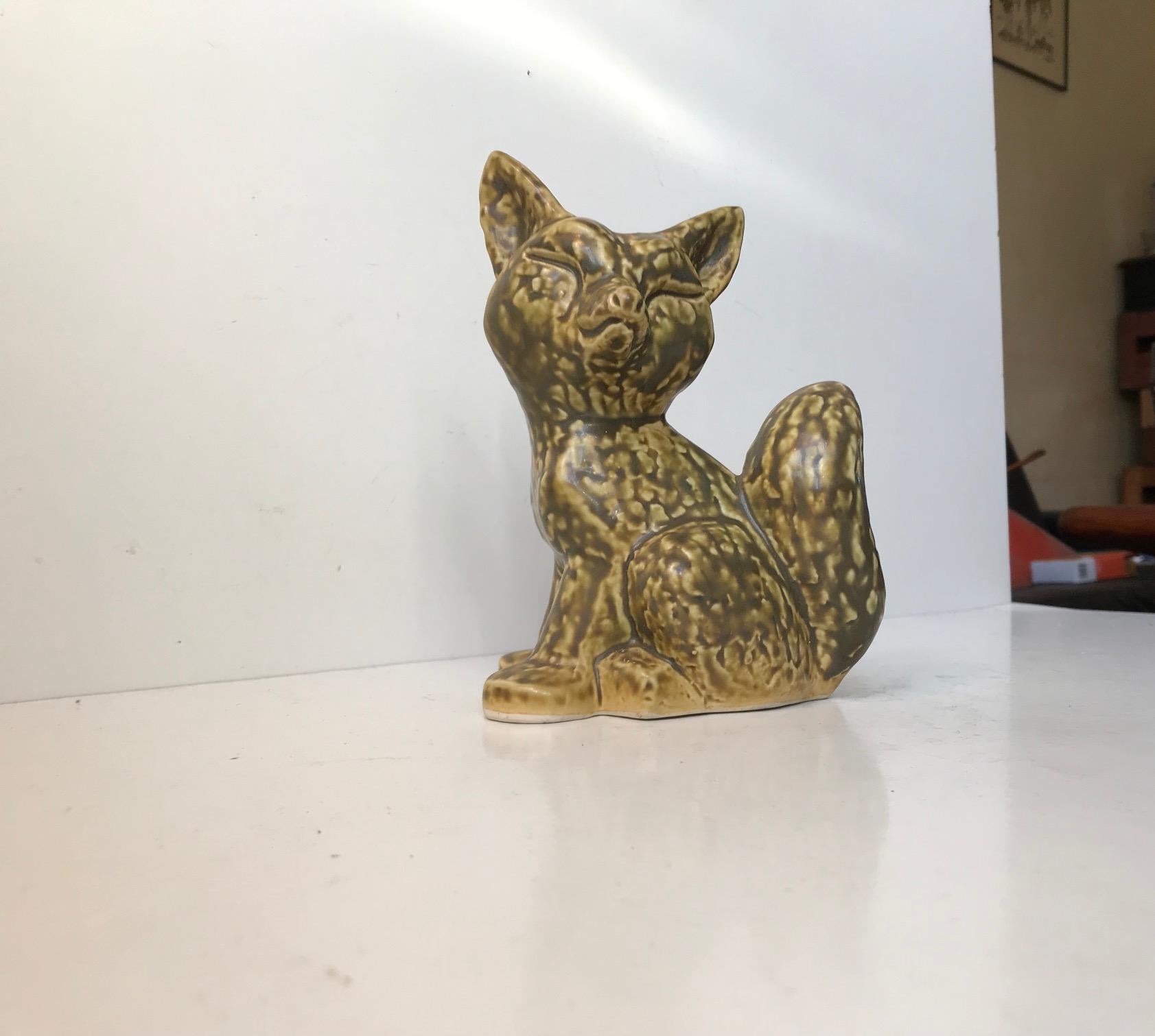 Cette charmante figurine de renard en céramique est recouverte d'une glaçure douce et subtile de couleur vert olive sur un fond jaune pastel. Il a été conçu et fabriqué par Kaare Berven Fjeldsaa's dans son studio, alias KBF, en Norvège dans les