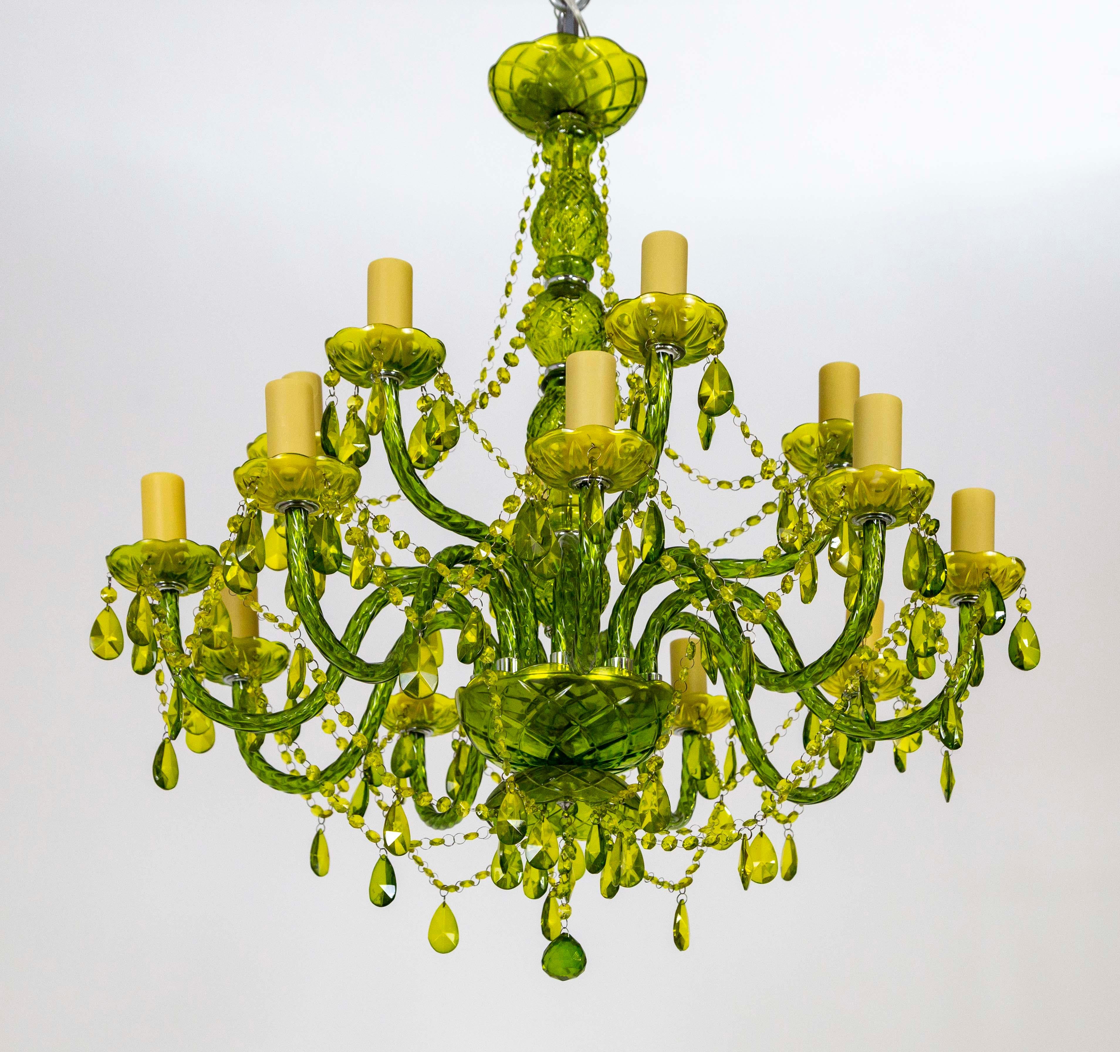 A green, candlestick-style chandelier with two tiers of curving arms, honeycomb-colored candle covers, and crystal garlands. The body is comprised of green-tinted glass with glass and acrylic crystals. 36” height x 30” width/depth. 

We offer UL