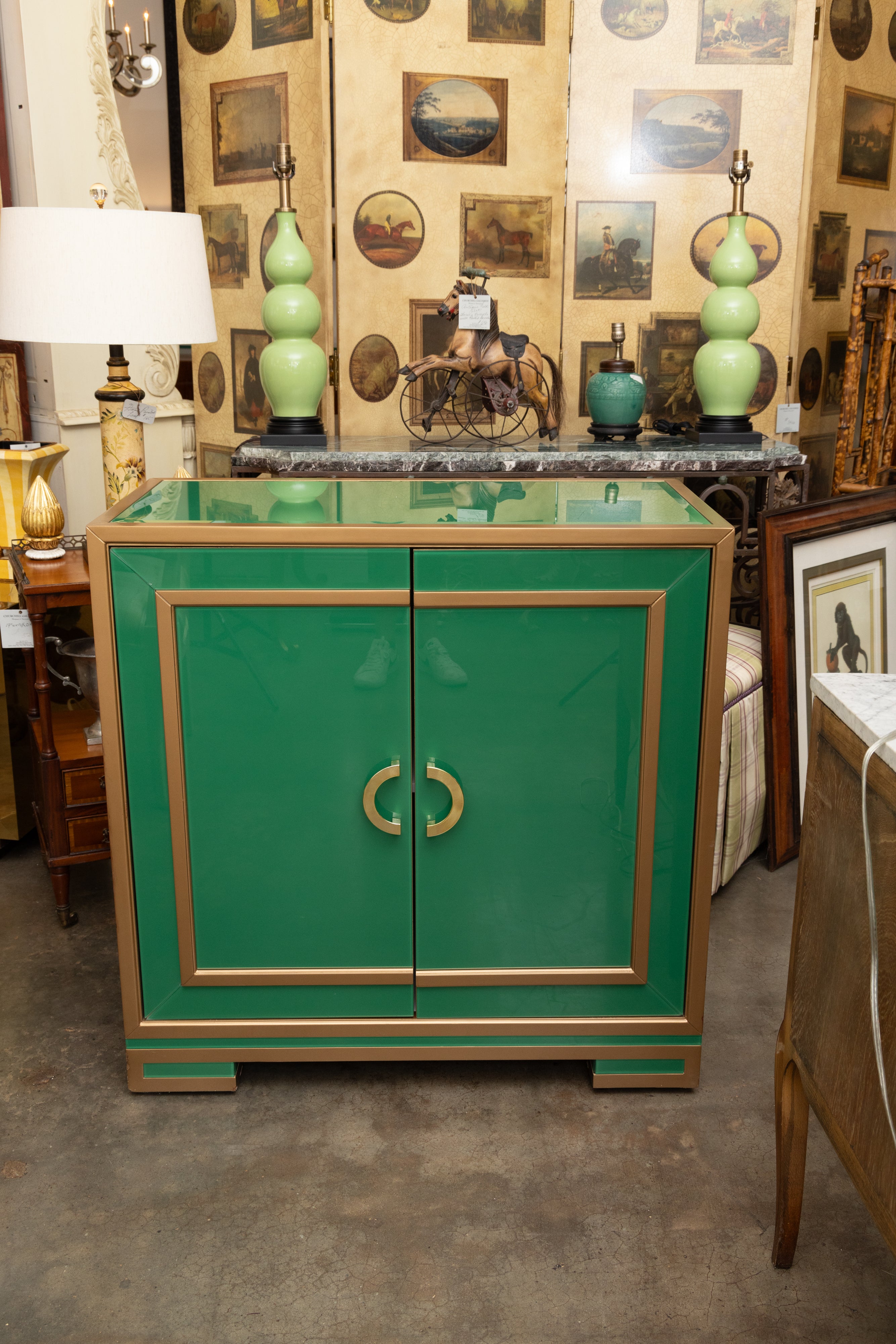 This is a very unique two-door cabinet comprised of green glass with brass trim and hardware, situated on small block feet with doors opening to reveal interior shelving.