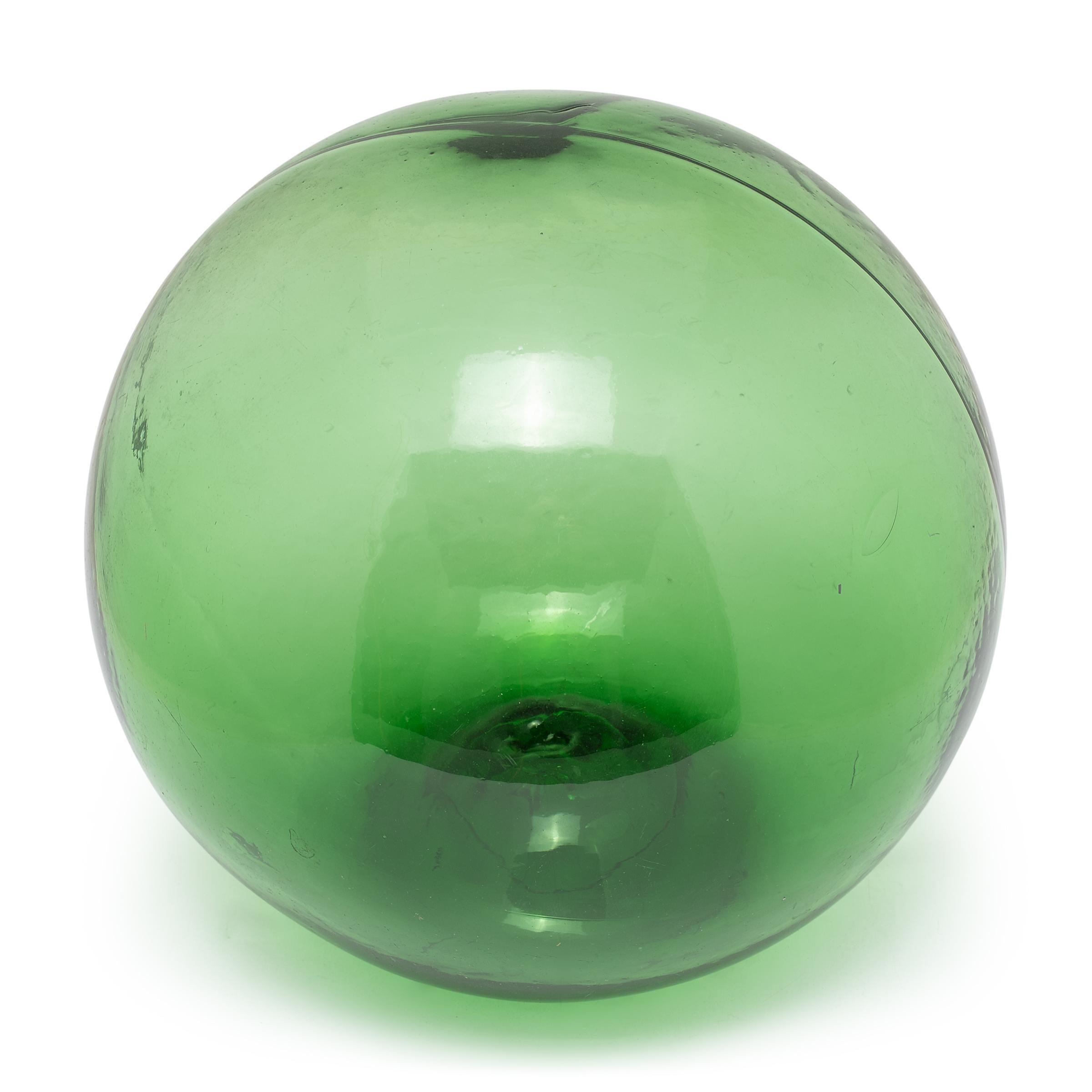 This beautiful green sphere is an early 20th century glass float used by fishermen to keep their fishing nets or droplines afloat in the ocean. The hollow float would have been encased by a rope netting and used just like a modern buoy. Because