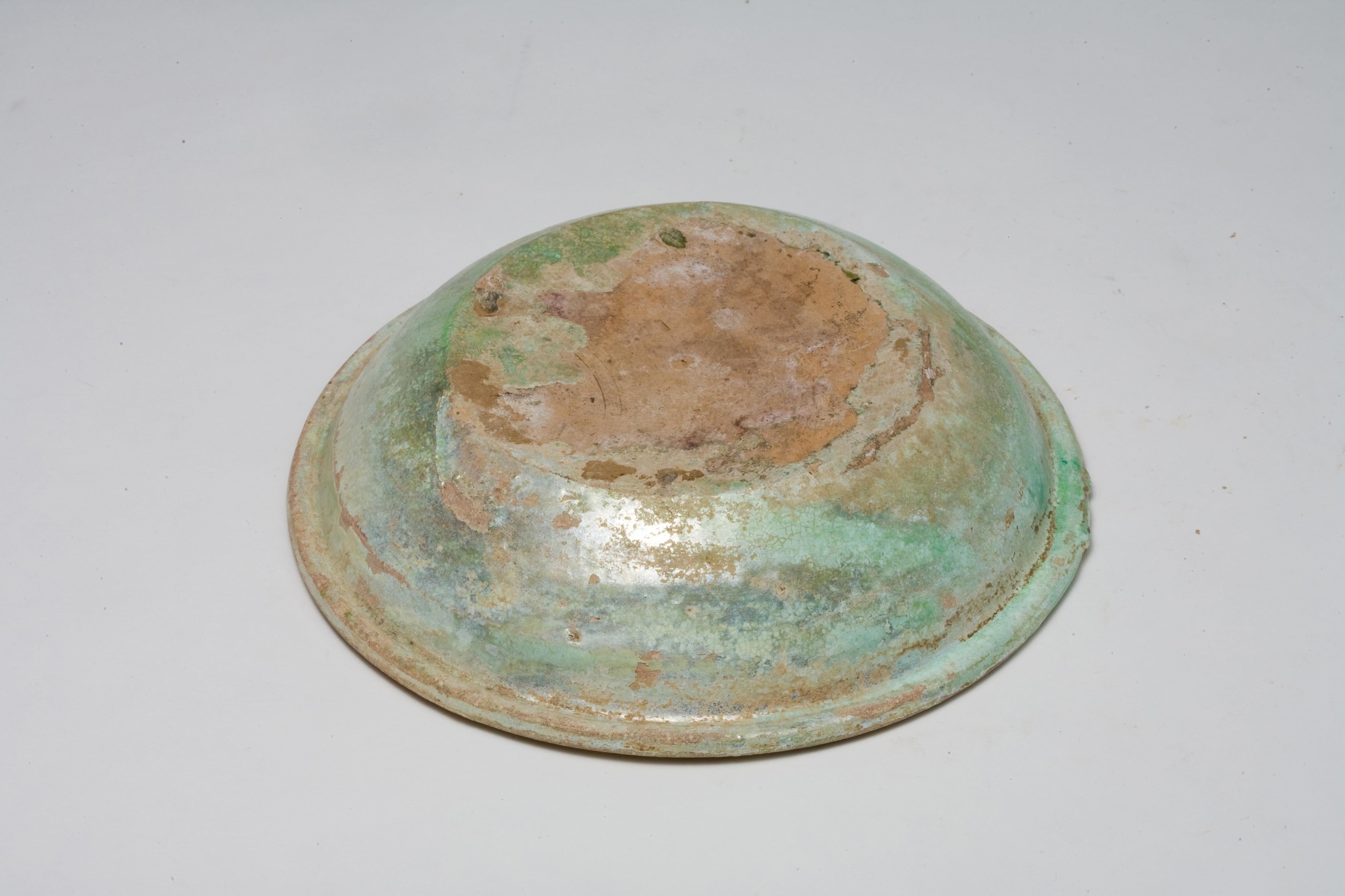 This Han Dynasty green-glazed dish exhibits significant signs of wear, indicative of its age and the long passage of time it has witnessed. The glaze, once vibrant, now shows substantial corrosion and deterioration, revealing the delicate nature of