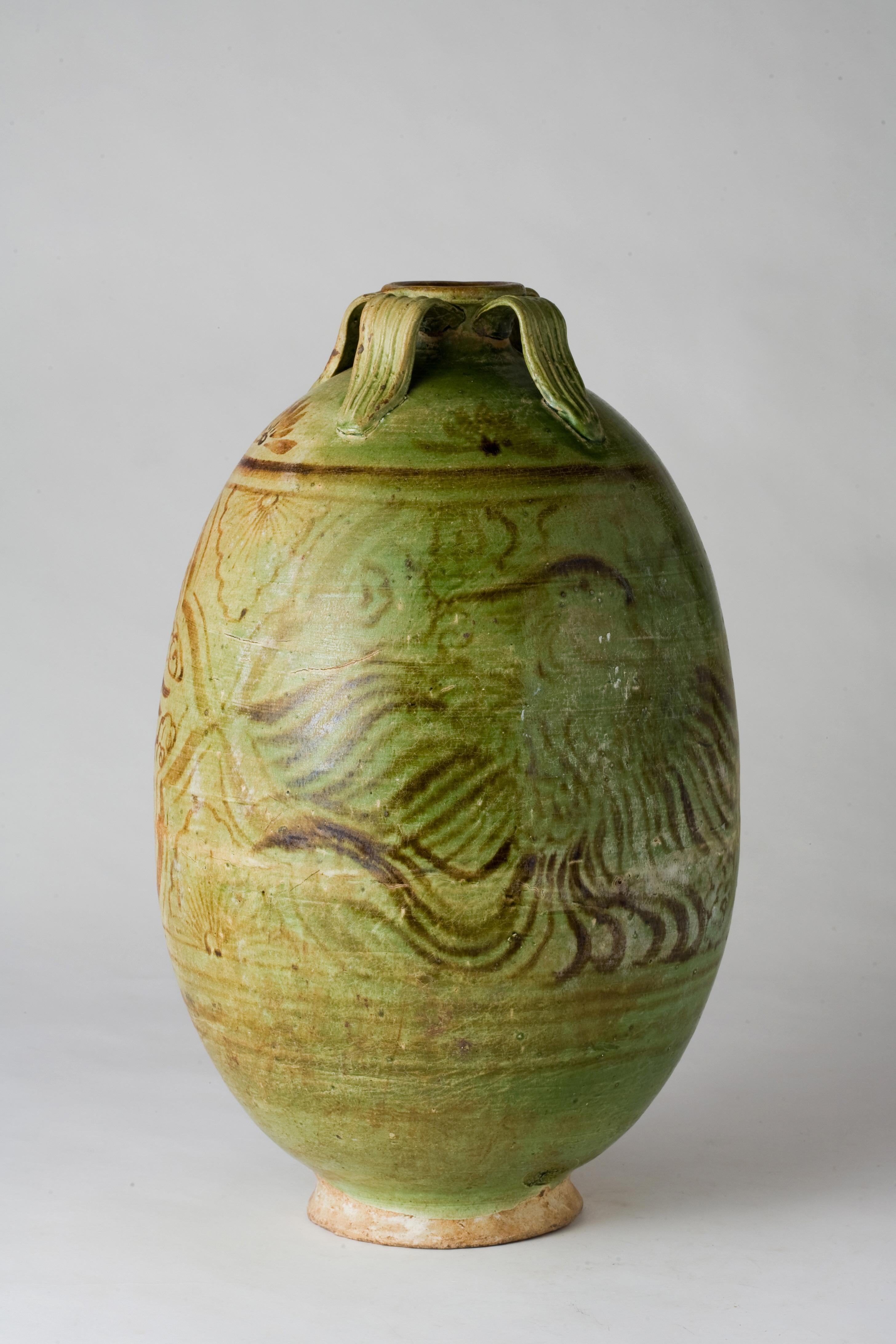 The vessel has an overall oval shape, characterized by smooth curves that transition naturally from the rim to the body. The upper part of the jar narrows slightly, with four handles arranged around the rim. The glaze exhibits a pale green hue