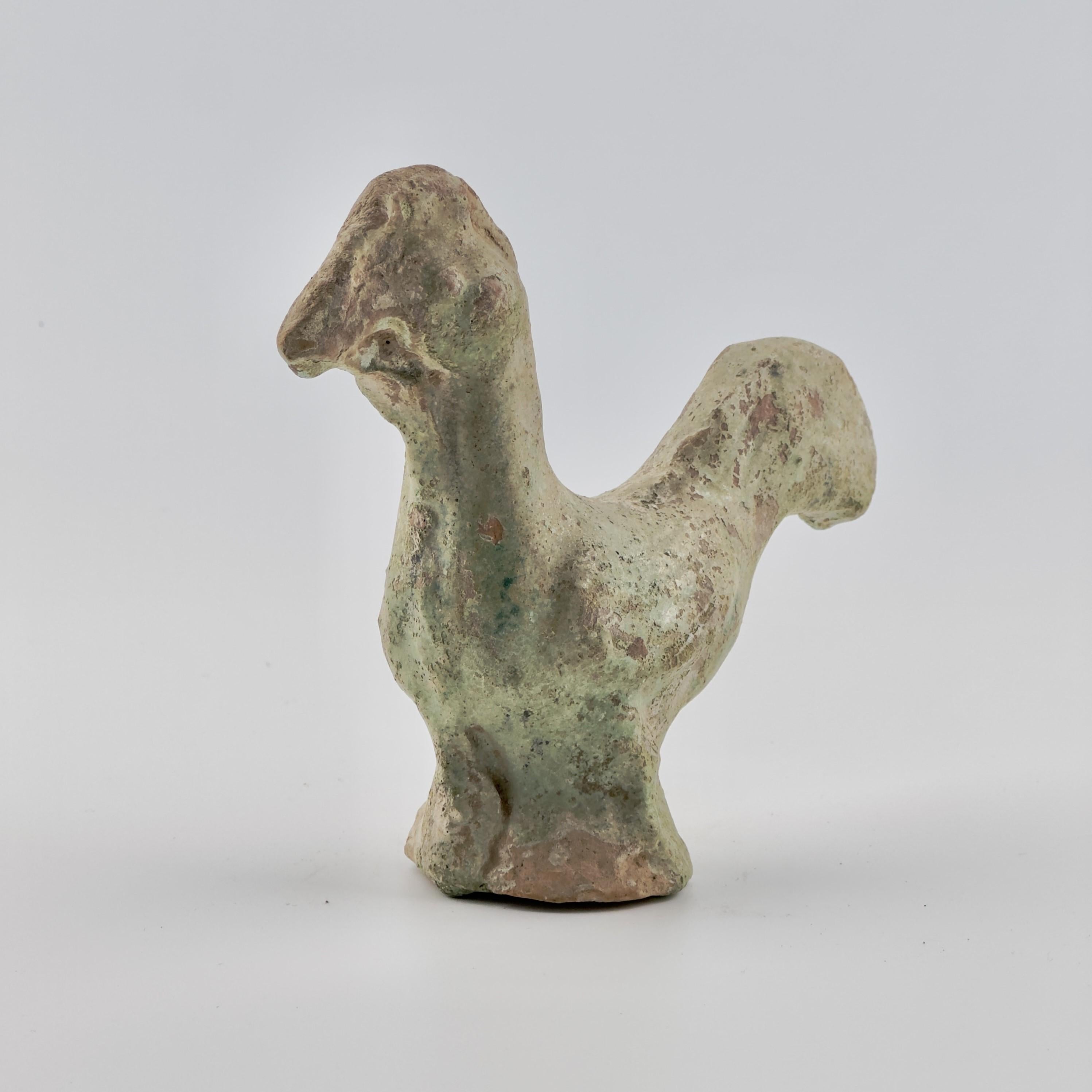 The head is rounded, with minimal detailing of the beak, eyes, and comb. The neck is thick and solid, seamlessly transitioning into the body, which appears sturdy and compact, giving the figure a sense of stability.

The most prominent feature of