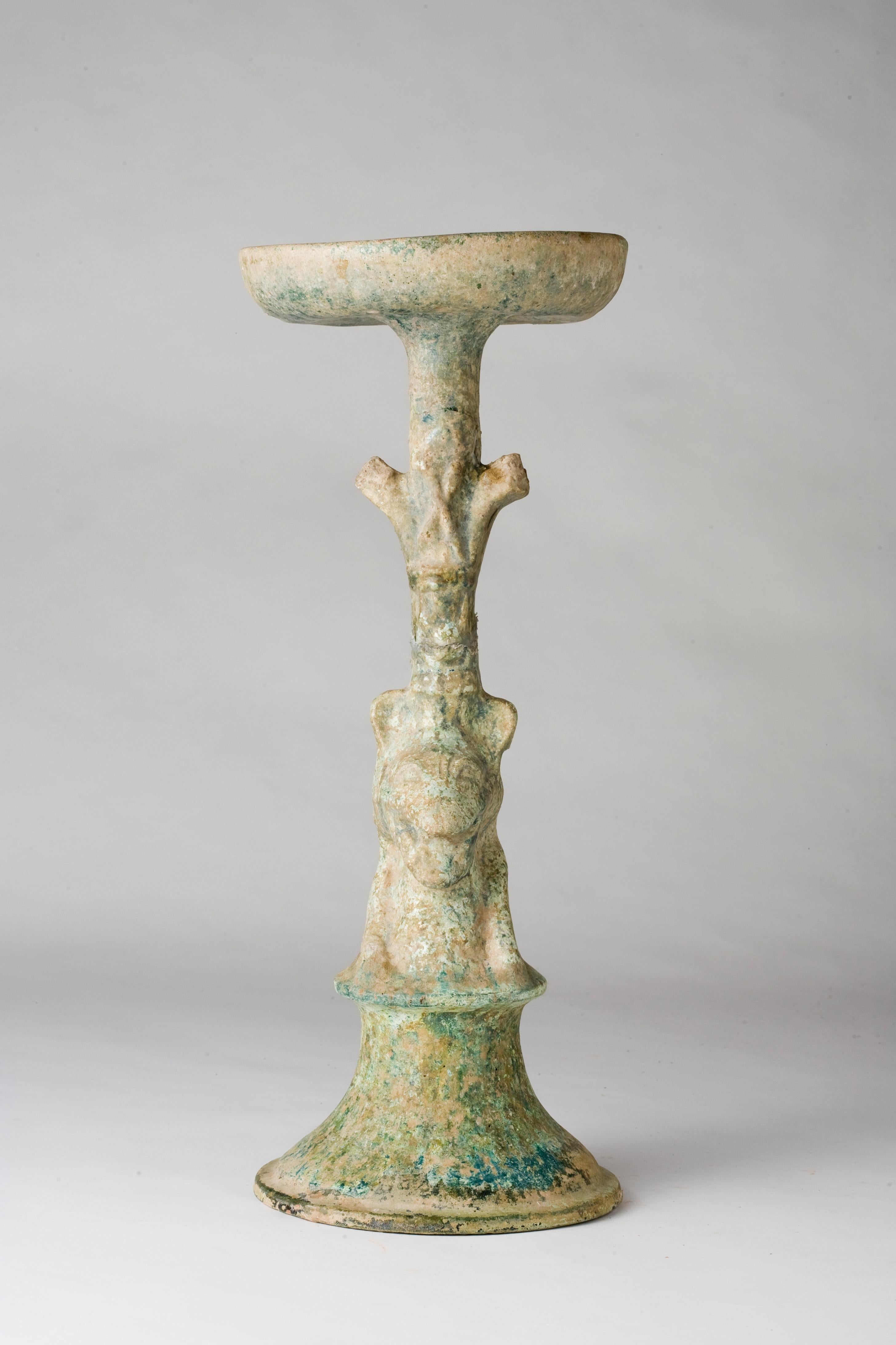 The upper section of the vessel is broad and flat, intended to support a candle or an oil lamp, while the stem and base are robust, designed for stability and durability. The surface is coated with a green glaze, which has matured over centuries to