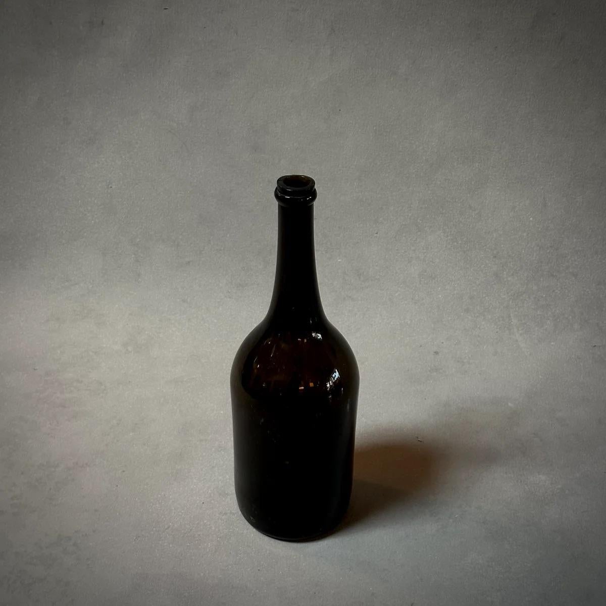 Ces bouteilles en verre soufflé à la main, d'une teinte olive profonde, sont un exemple de charme rustique et de savoir-faire artisanal. Chaque bouteille, unique dans sa forme grâce au processus de soufflage à la main, a de multiples fonctions :