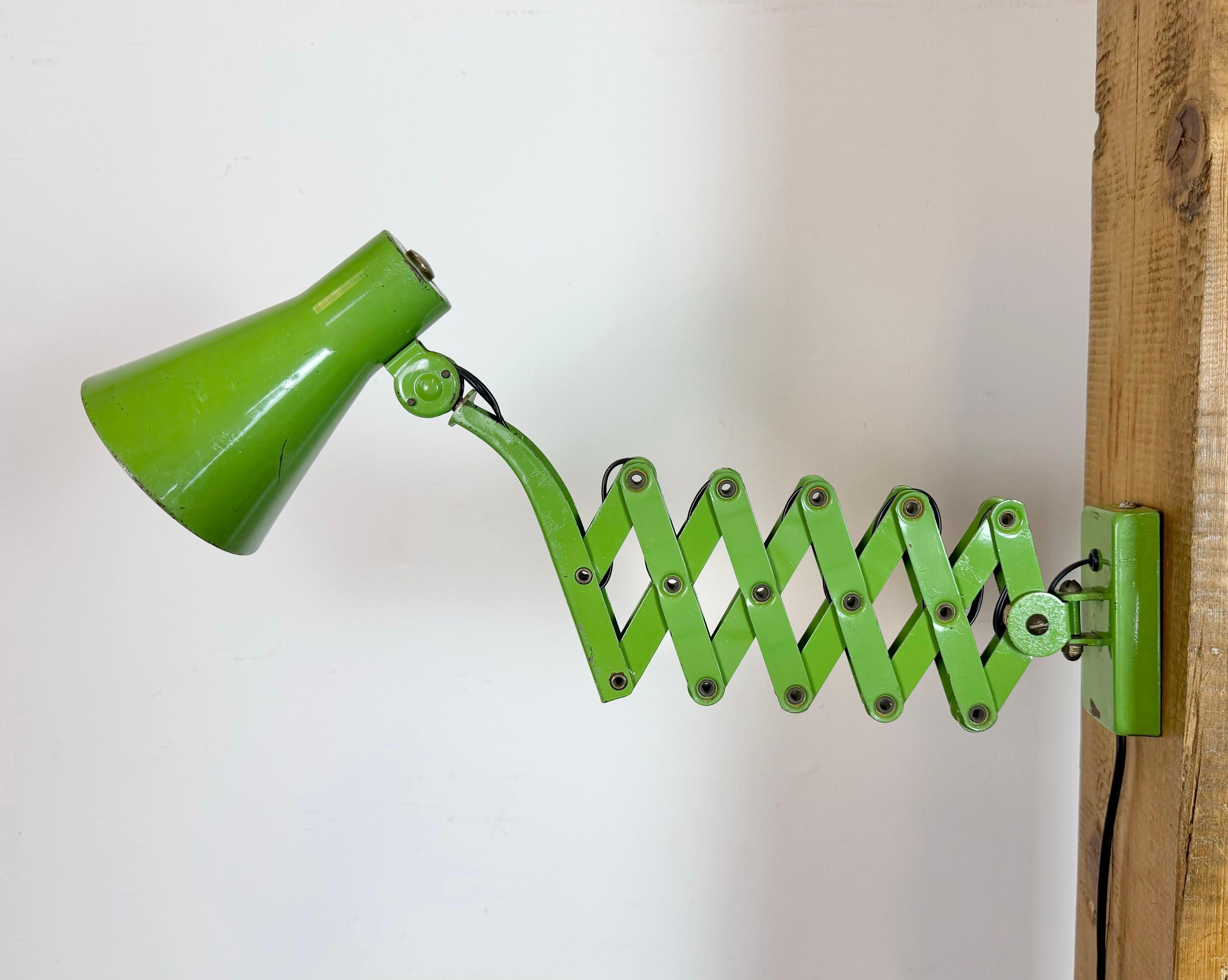 This vintage industrial workshop scissor wall light was made by Kaiser Leuchten in Germany during the 1960s. It features an adjustable green metal shade, a green iron scissior arm is extendable and can be turned sideways. The socket requires