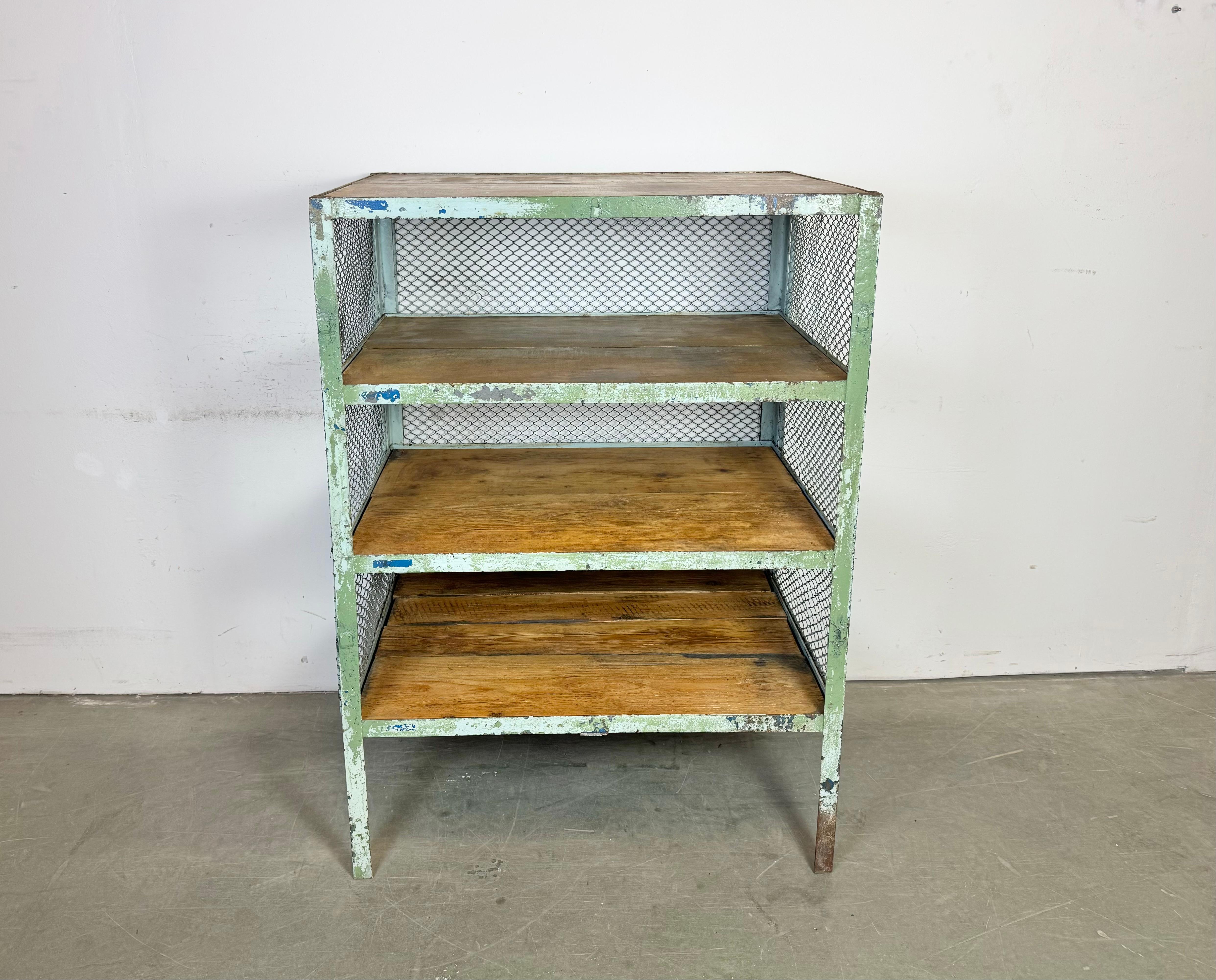 Scaffale industriale degli anni '60. Presenta una struttura in ferro verde con lati e retro in rete di ferro e quattro ripiani in legno.