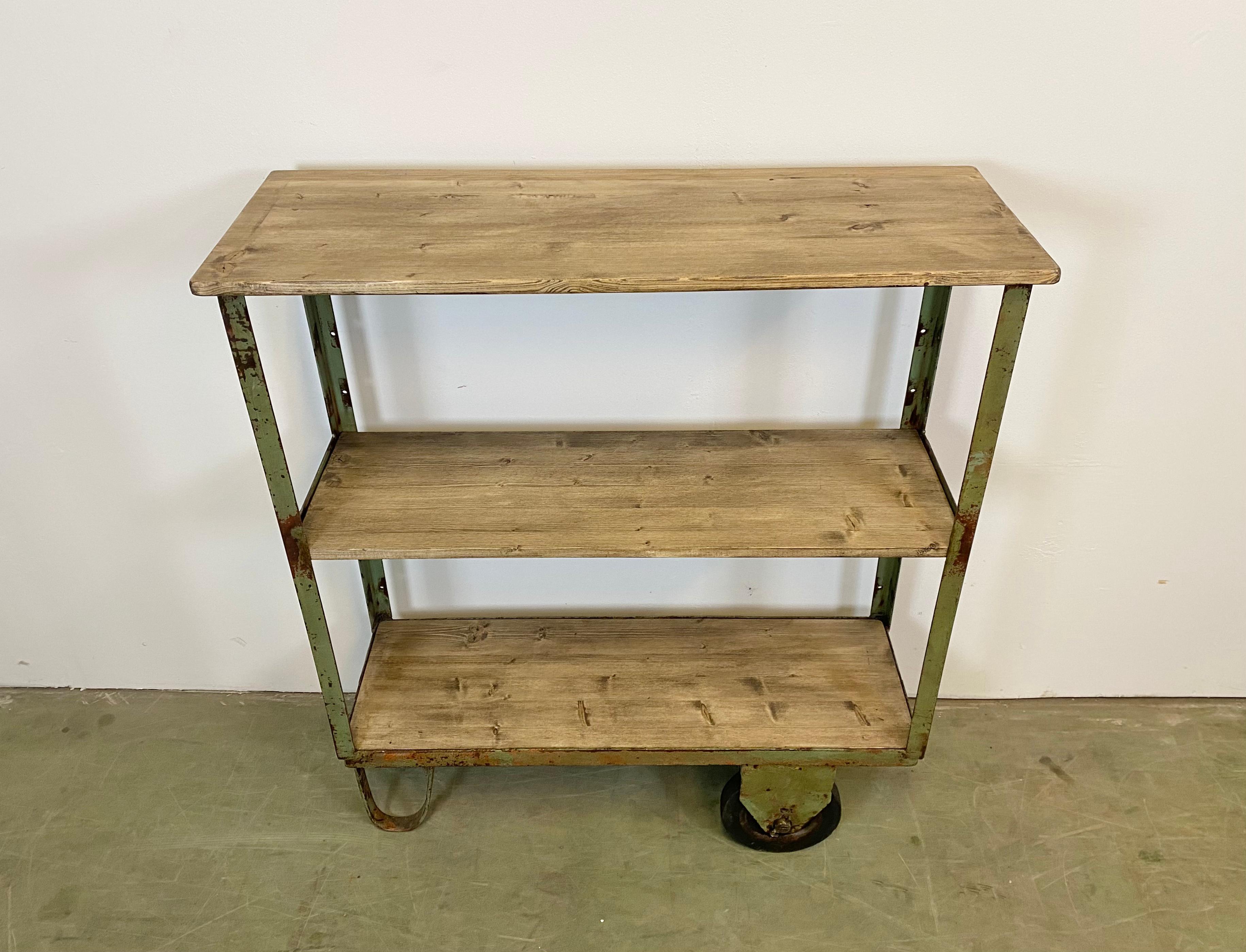 Industrial shelf from the 1960s. It features a green iron construction, three wooden shelves and two original wheels. The weight of the shelf is 32 kg.