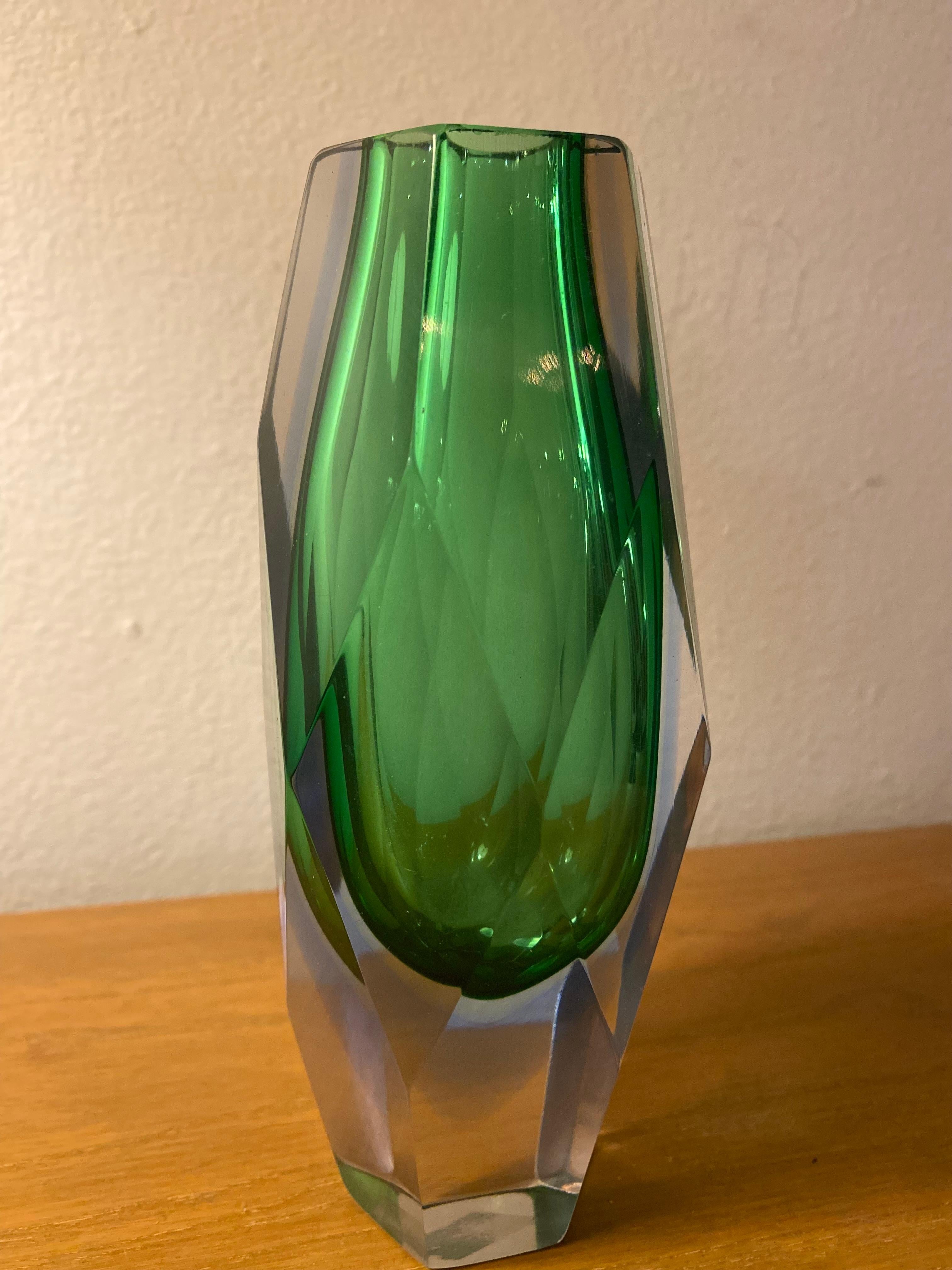 Este jarrón de Murano está elaborado en el estilo Sommerso, desarrollado por el diseñador Flavio Poli, conocido por su enfoque innovador del diseño en vidrio. El jarrón presenta una forma facetada en cristal de Murano verde intenso, con un efecto de