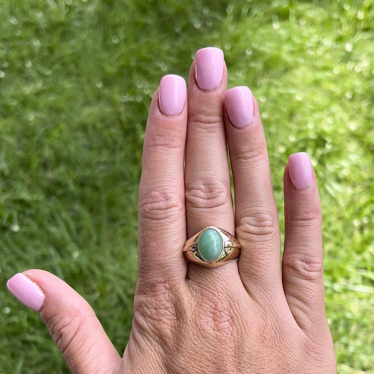Oval shape cabochon green jade ring, bezel set in 14k yellow gold. The Jade measures approximately 13.27 mm x 9.94 mm x 5.60 mm with an estimated weight of 6.67 carats. The ring has a rounded tapered shank with a raised design element on both