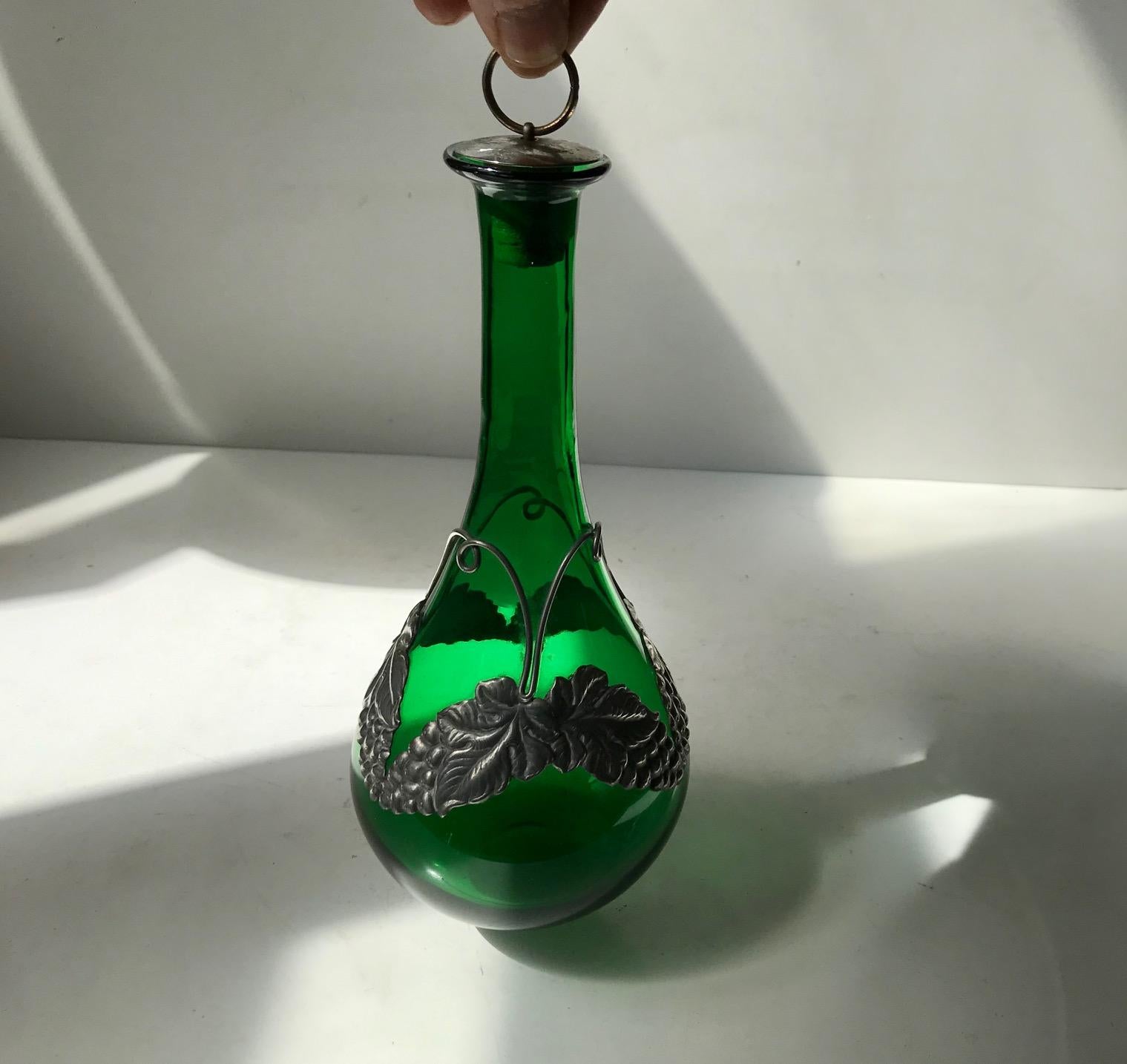 Organically shaped handblown decanter with a floral decoration in pewter. This decanter was made at Holmegaard in Denmark during the early 192os. The art nouveau pewter belt was created by a danish silversmith in the same period. This item is