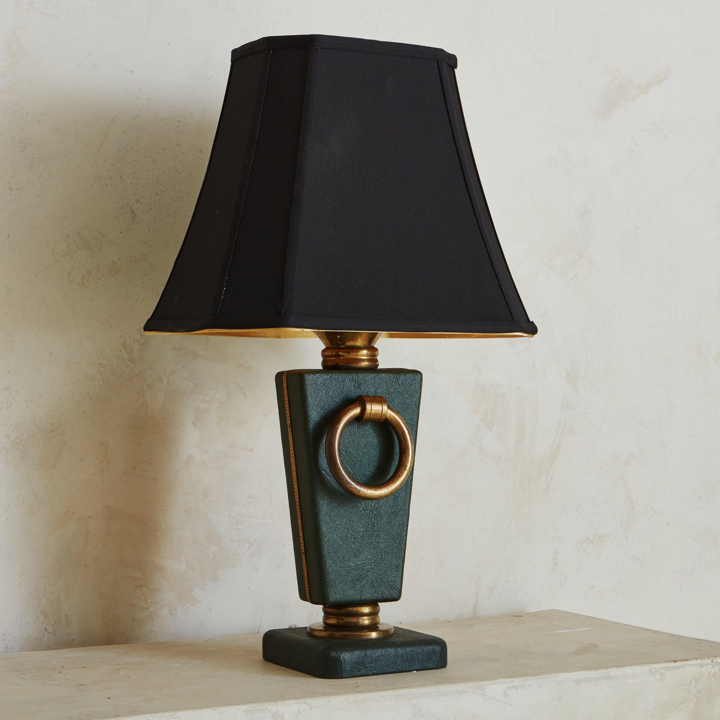A vintage table lamp clad in green leather with two decorative circular brass details on either side. This lamp has a subtle red leather trim with gold greek key motifs and a square pedestal base. Sourced in France, 1960s. 
 

 DIMENSIONS: 4.75