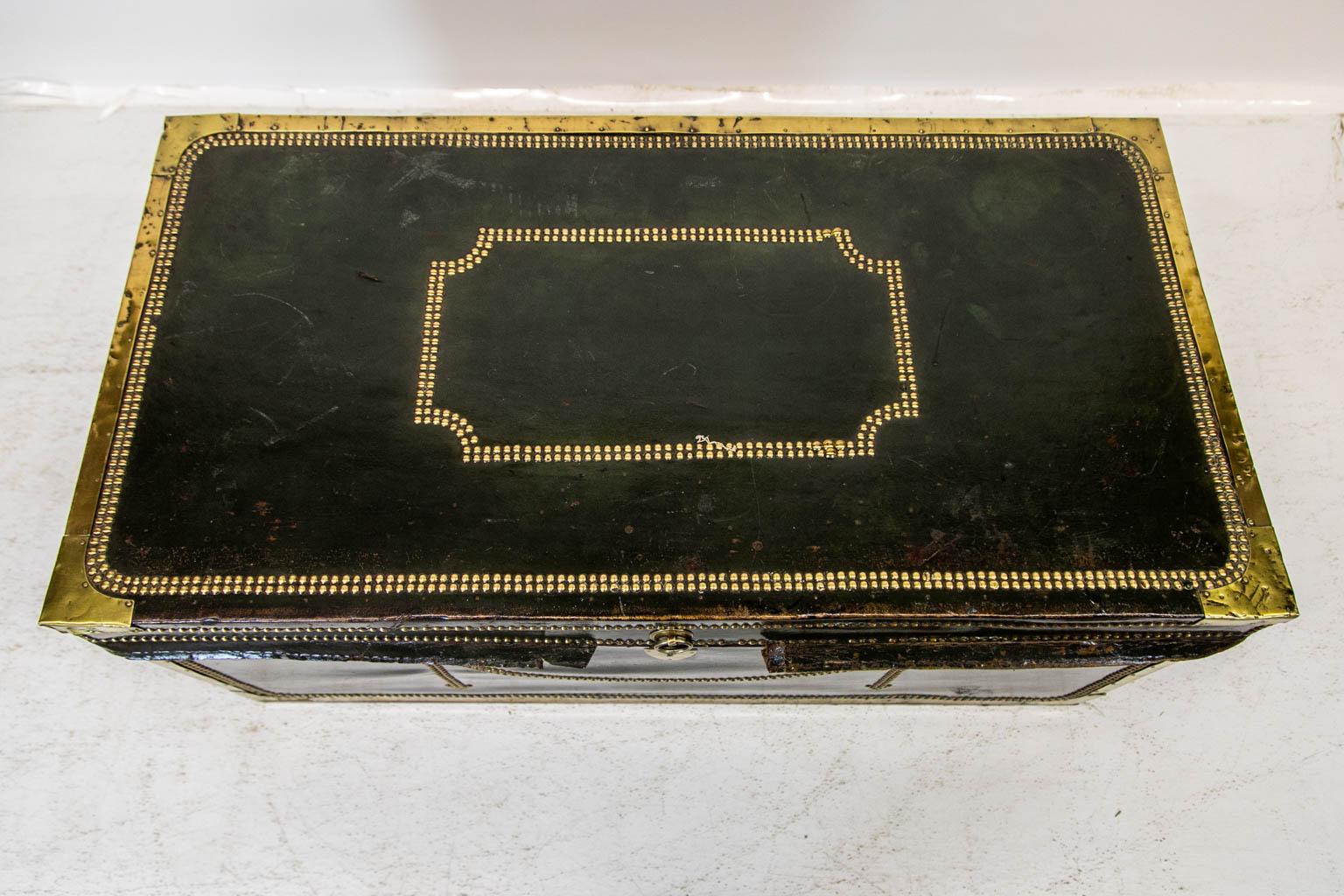 This trunk has repeating brass stud work that frames the top with a studded panel. A few of the brass studs have been replaced and a few are missing. The top and edges have a solid brass border except for the front top edge which was removed at some