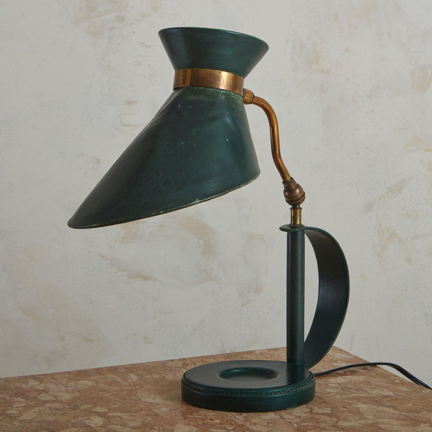 A 1950s desk lamp in the style of Jacques Adnet featuring a sculptural shade and body clad in green leather with stitch detailing. It has a curved, adjustable brass stem with a beautiful patina. This lamp has a circular catchall detail on the base