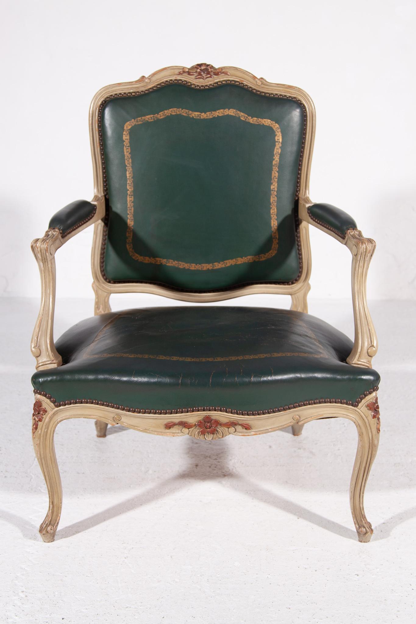 Ein Cabrio-Sessel im Louis XV-Stil aus weiß lackiertem Holz, der auf vier Cabriole-Beinen steht, die mit geschnitzten Blättern und Blumen verziert sind. Sitzfläche und Rückenlehne sind mit Messingnägeln versehen und mit grün patiniertem Leder