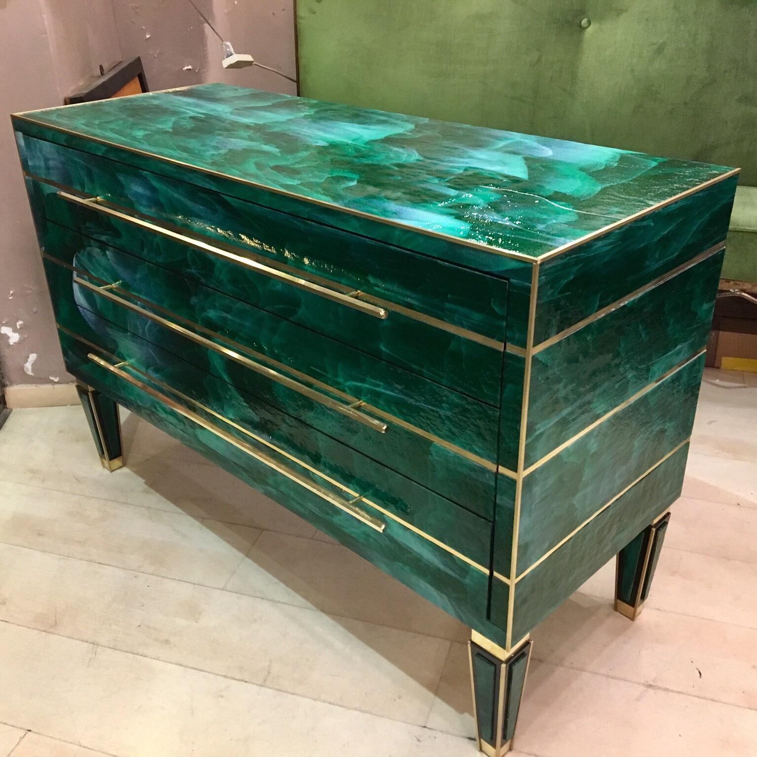 This green opaline glass chest of drawers presents typical brass inlays from the 1980s, brass handles with hexagonal section, pyramid-shaped legs, three drawers. 

The opaline glass that covers the furniture is made of a melange of green and light