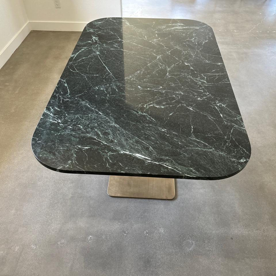 Sleek and modern pedestal dinning table or console. The green marble slab rests on top of a brushed brass pedestal base.  This is a very sturdy and handsome piece!.
Made in Los Angeles