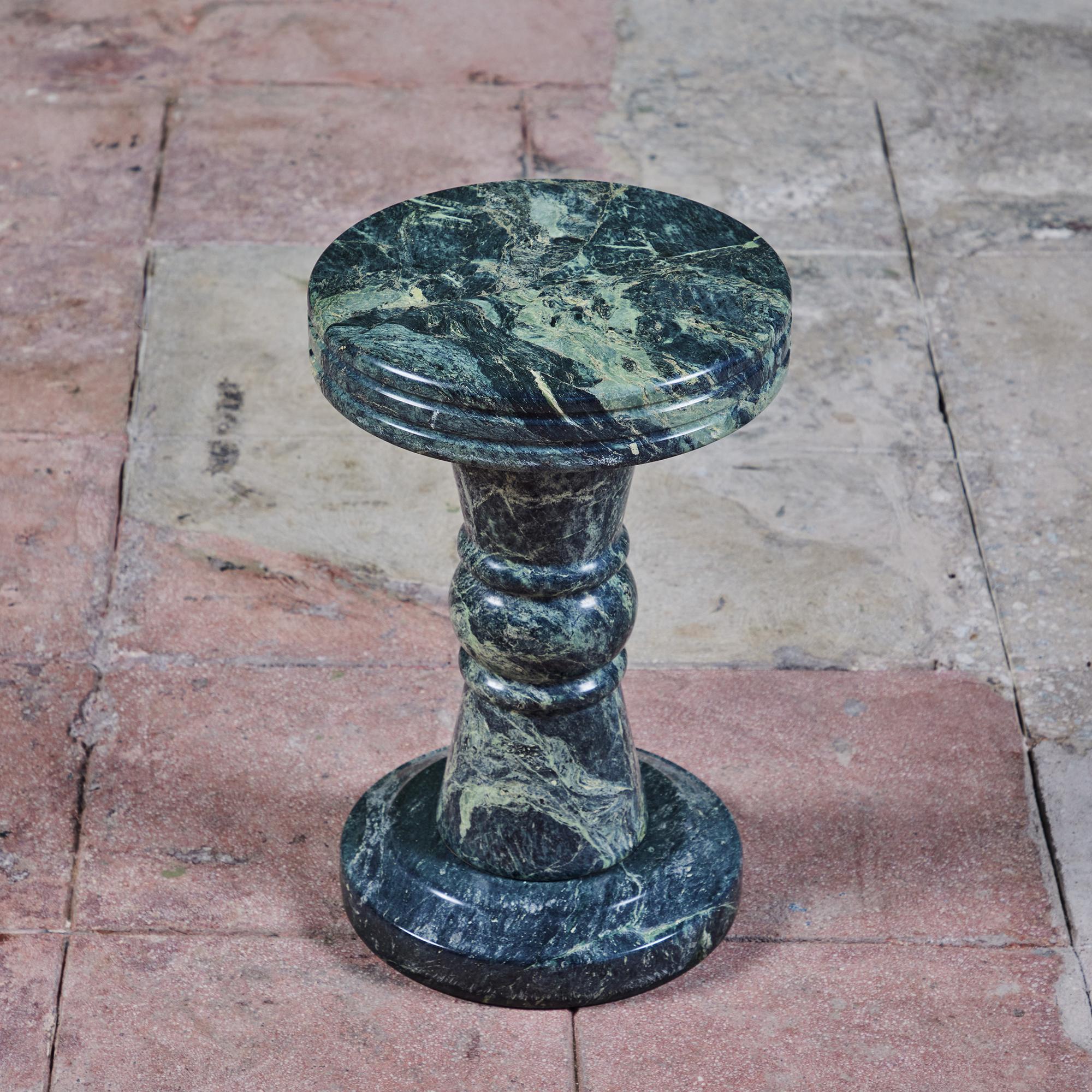 Roman style green marble pedestal side table or stool. The table features a rich green body with varying tones of green veining throughout. The table top as two incised lines around the outer rim of the table and a circular base that mimics the top.