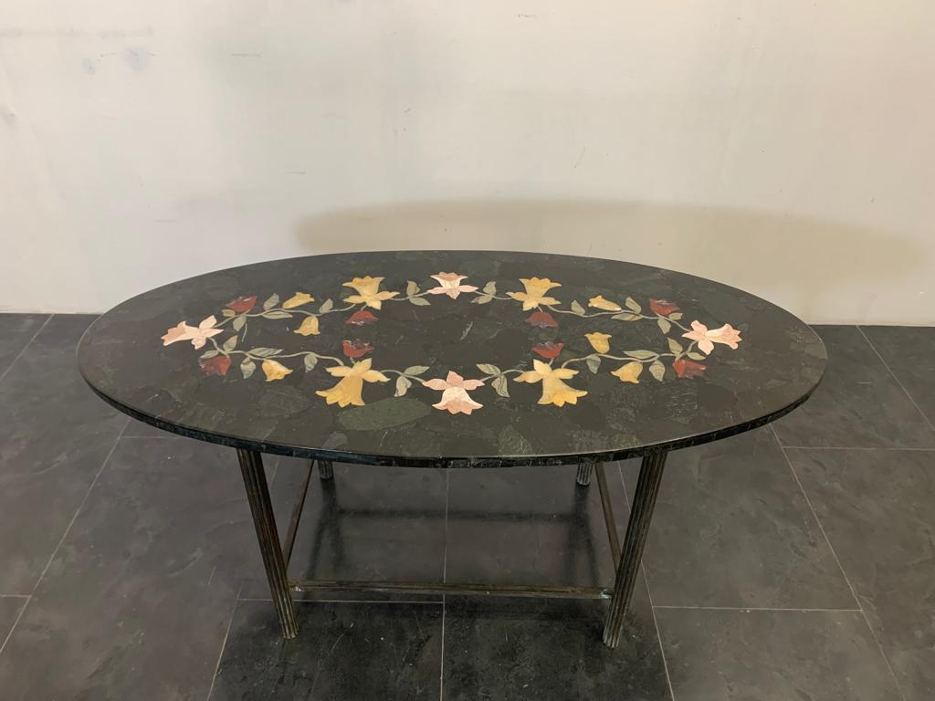 Table ovale de style Art déco. Base composée de 4 pieds cannelés en cuivre patiné vert. Dessus plaqué sur scagliola en plaques filiformes de marbre vert Alpi sélectionné foncé. Au centre se trouve une incrustation en marbre polychrome à thème