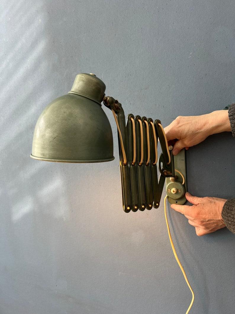 Metal scissor wall lamp in gray - green colour. The scissor arm allows you to adjust the lamp's position to suit your needs. Also the shade itself can be easily adjusted in position. The lamp requires an E27/26 (standard) lightbulb and currently has