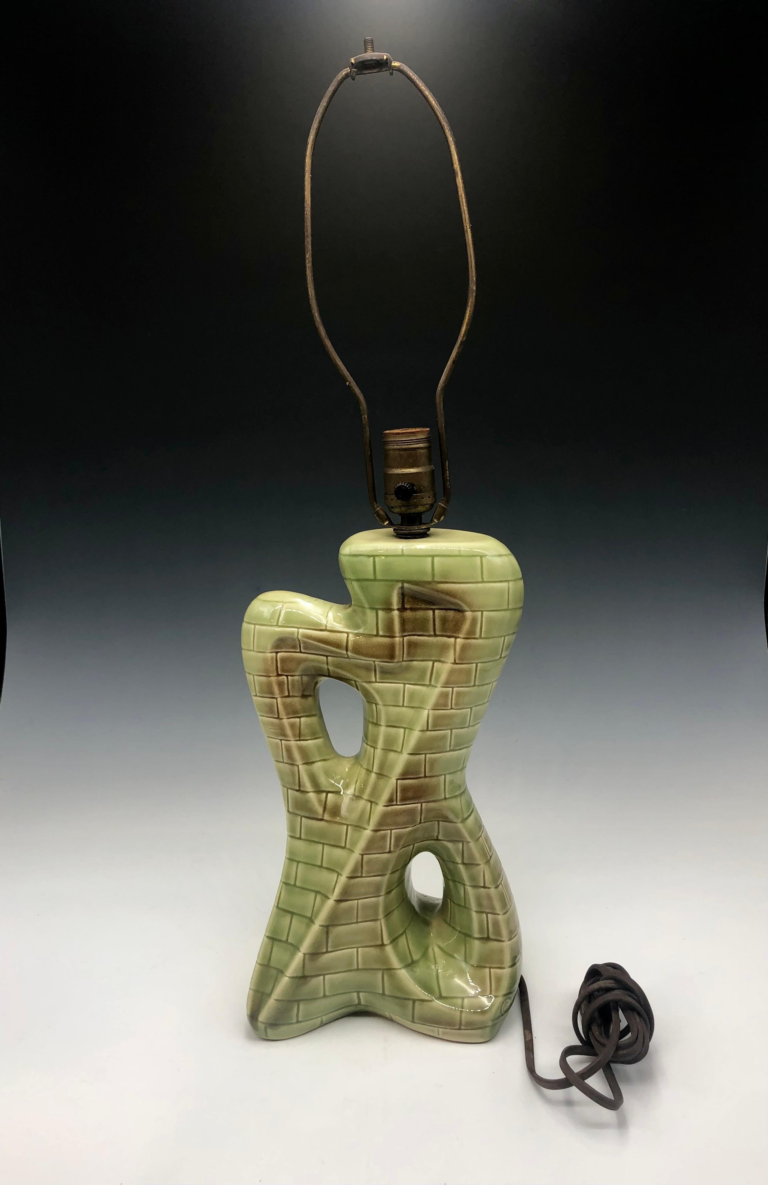 This striking mid-century ceramic table lamp embodies the bold artistic spirit of the 1950s–60s, merging sculptural form with playful surface design. The body features an asymmetrical, abstract silhouette with dynamic cut-out details, giving it a
