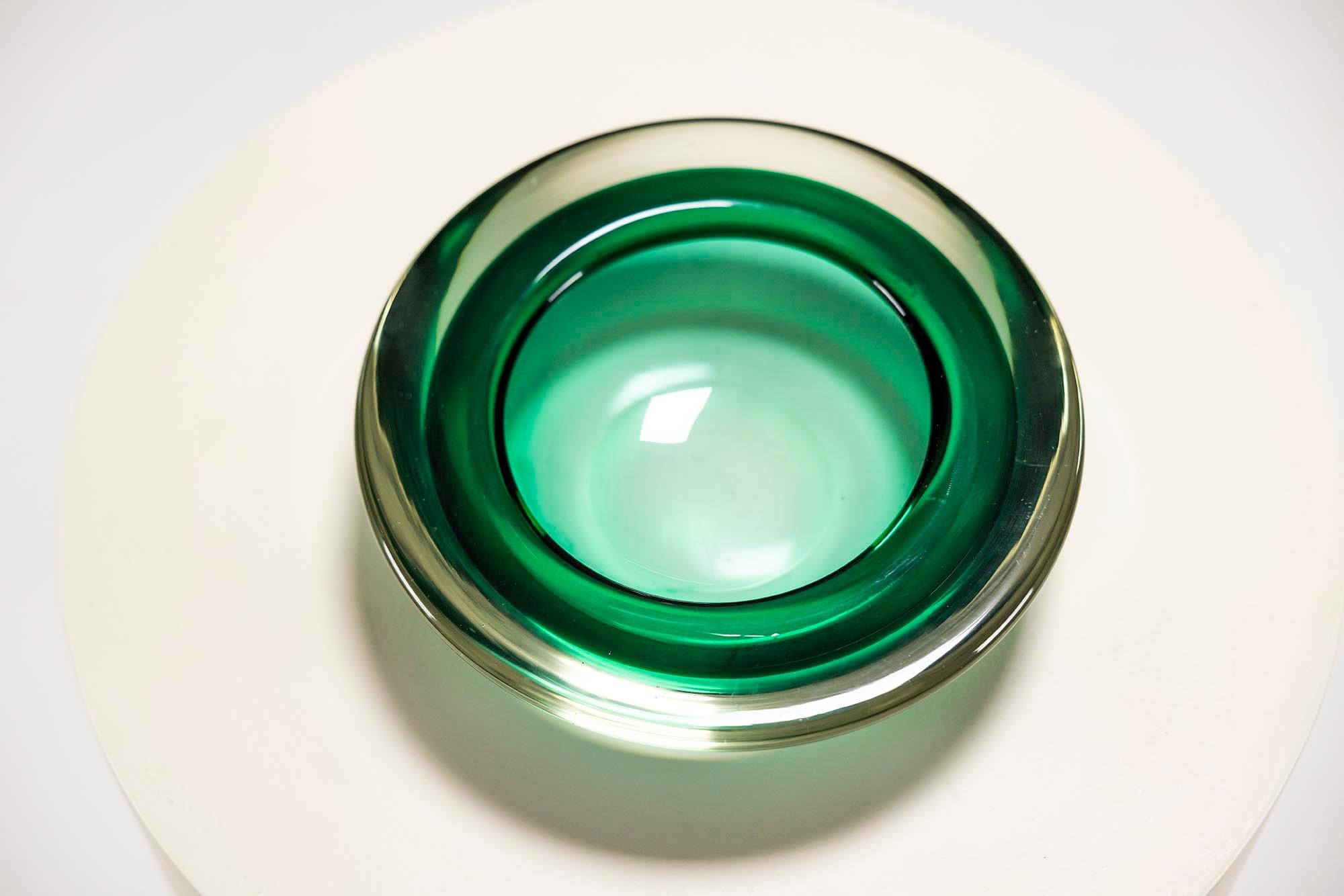 This Murano glass bowl showcases the skill of Venetian glassmaking. Its deep green color draws attention, with the glass capturing and reflecting light naturally. The bowl's rounded form, with a slight inward curve, gives it a balanced and