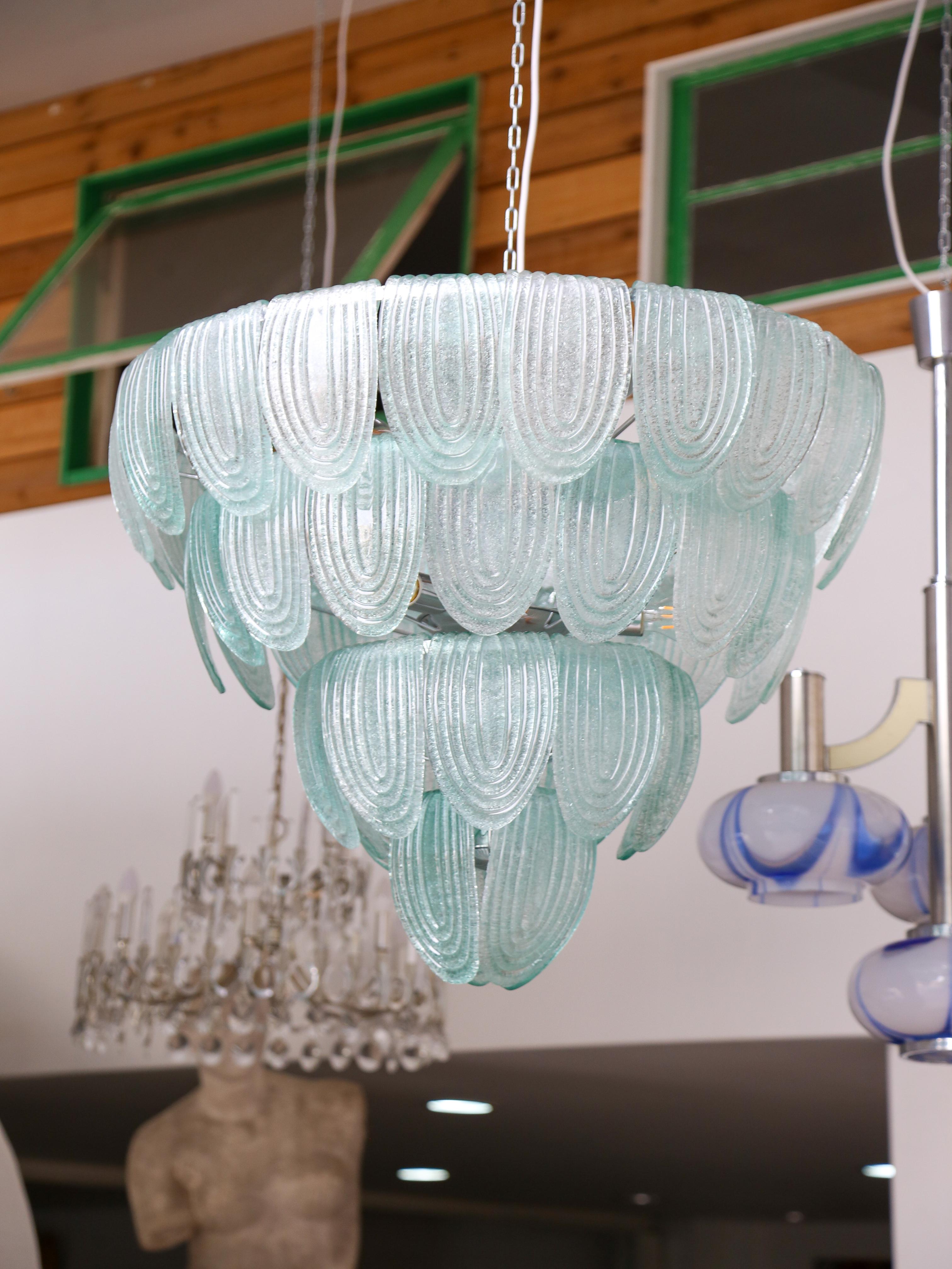 Kronleuchter aus grünem Murano-Glas mit einem Metallrahmen mit vier Ebenen von Sätteln und elf Glühbirnen im Inneren. (Die Gesamtzahl der Glassättel beträgt 54)
Dieser Kronleuchter ist nicht nur eine luxuriöse und elegante Leuchte, sondern auch ein