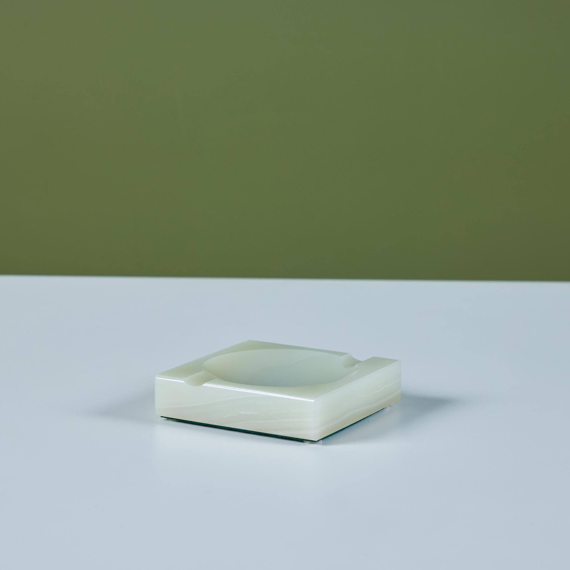 Polished square onyx ashtray features a soft green color with light cream veining around the sides. The piece has a circular dish center, and two cutouts for a cigarette. Though initially used as an ashtray, it can serve as a vide poche or