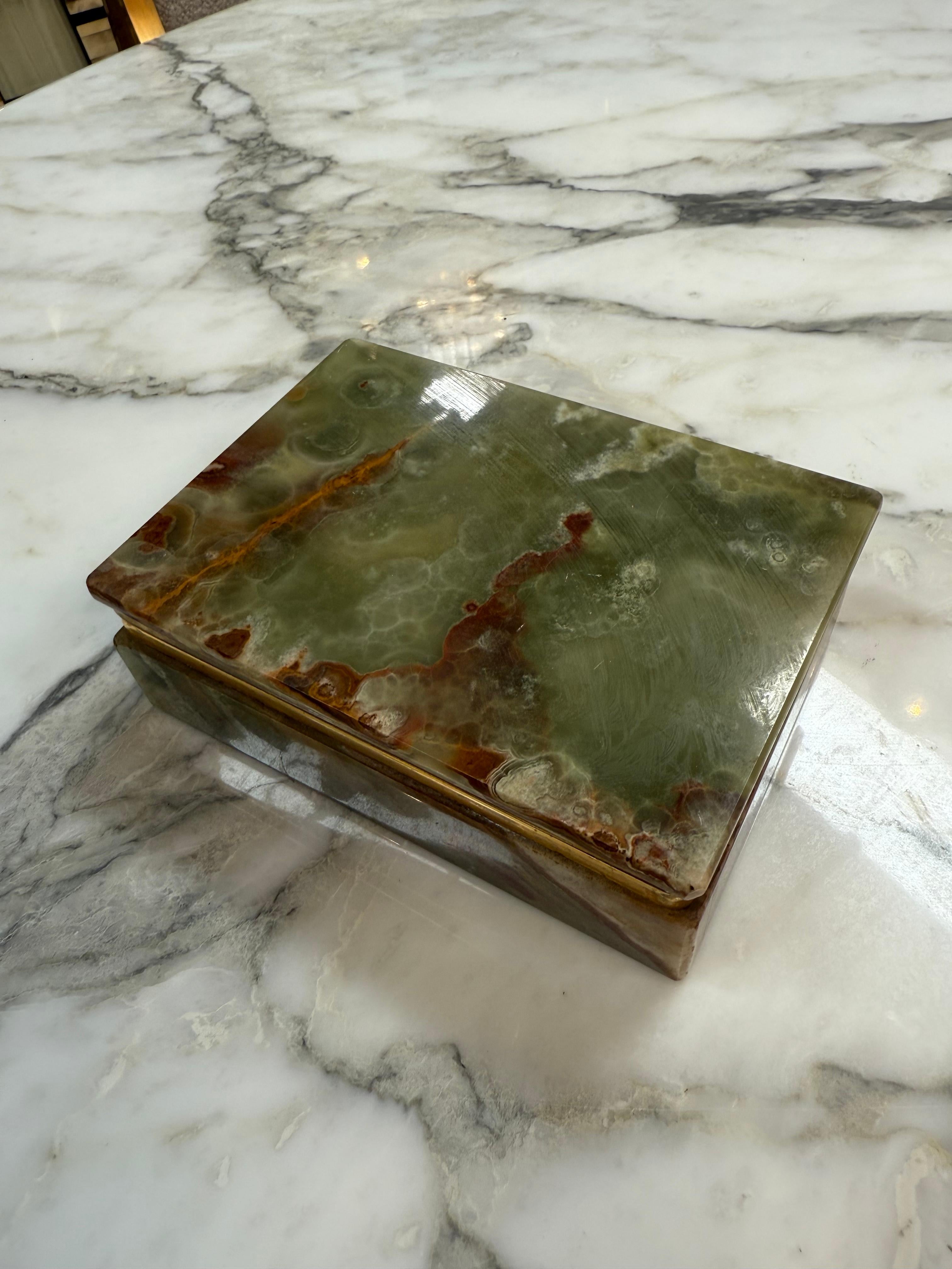 This rectangular vintage jewelry or trinket box is beautifully handcrafted from green onyx stone, showcasing the stone’s organic swirls and veining in rich tones of moss green, honey, and rust brown. The natural translucence of the onyx creates a