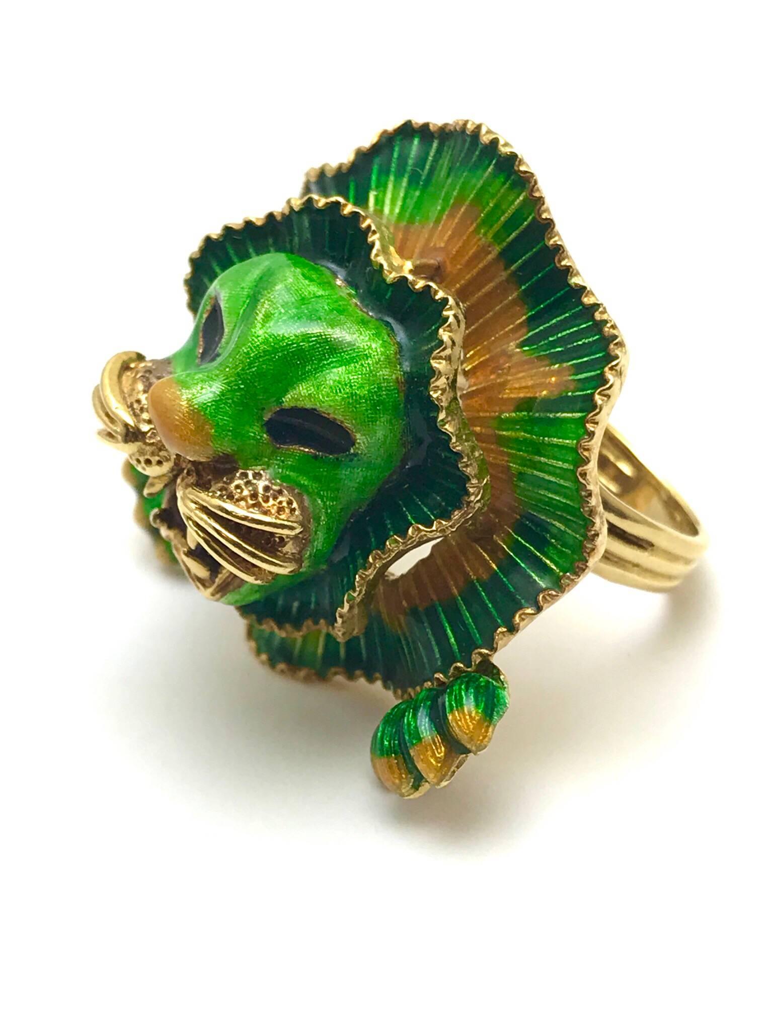 A green orange and red enamel 18 karat yellow gold lion cocktail ring.  The lions mane and paws are made up of the green and orange in a circular pattern of two tiers.  The mouth and whiskers are 18 karat yellow gold, with a red enamel tongue. 