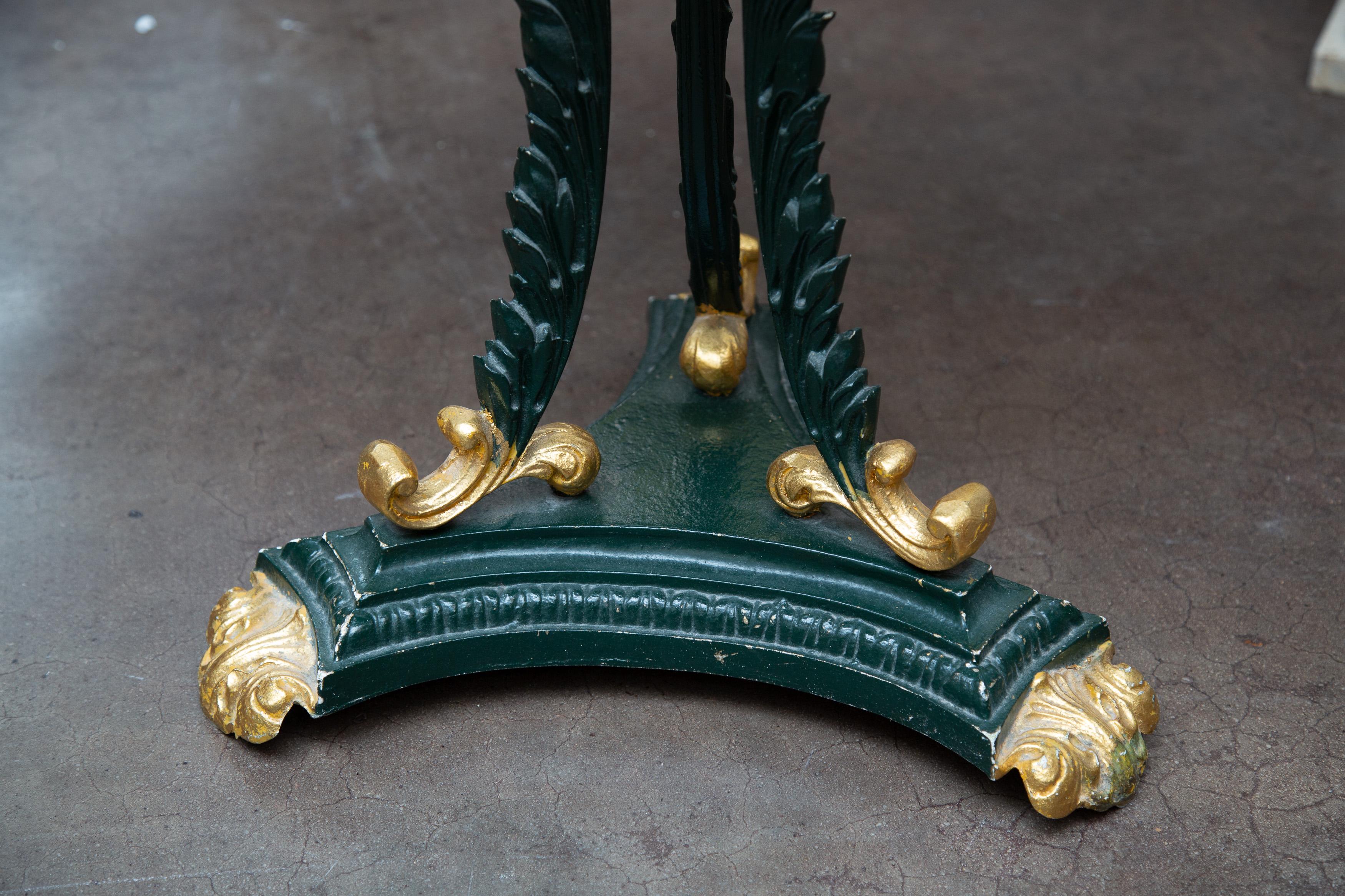 This is an attractive French green-painted and parcel gilt circular iron table. The travertine top is supported by three ornamental out-scrolling fronds situated on a triangular base.