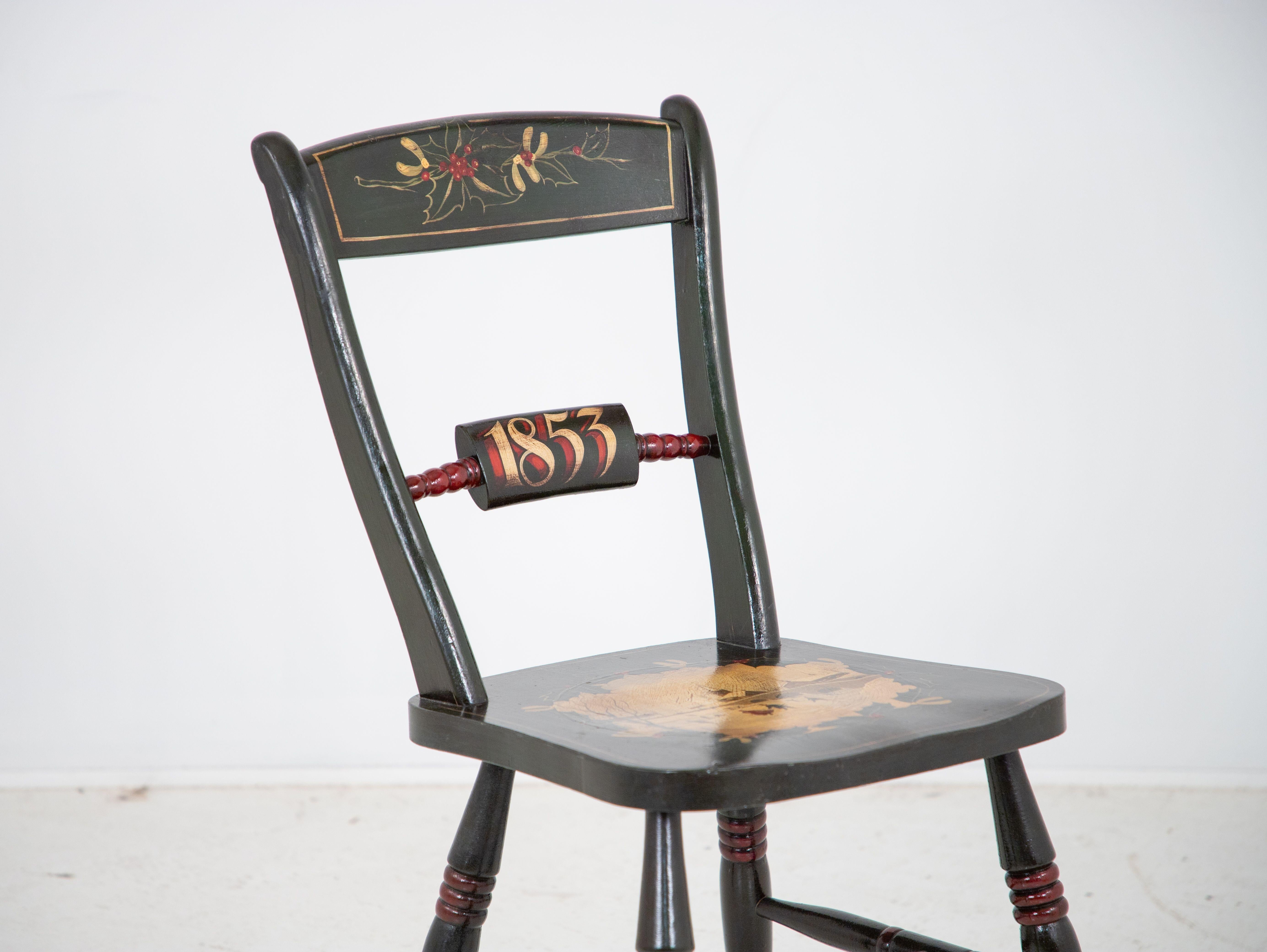 This antique side chair painted in green is a celebration of Christmas. The back features a holly and berry design and the year 1853 in red and gold. The seat is painted with a stunning winter scene featuring a frozen pond with skaters, a bridge,